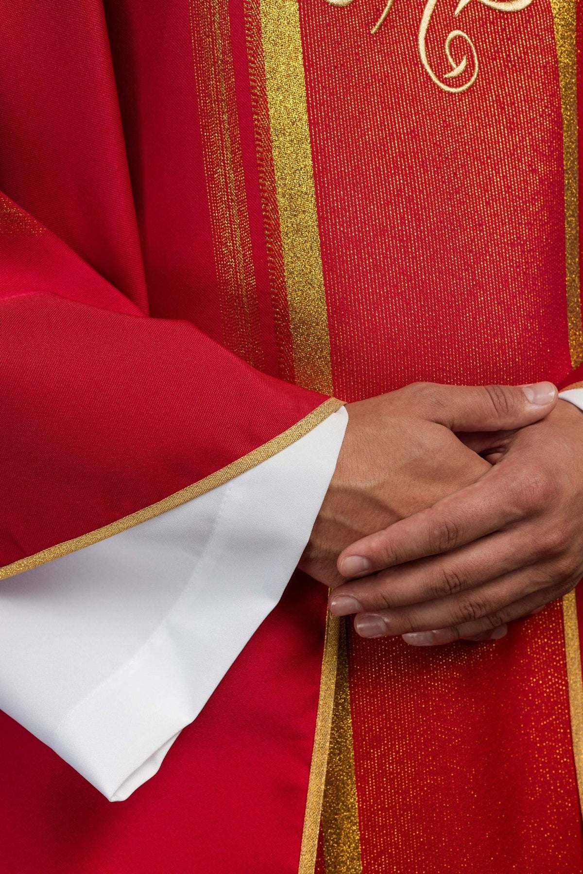 Red chasuble detail showing gold trim, red fabric and embroidered IHS design