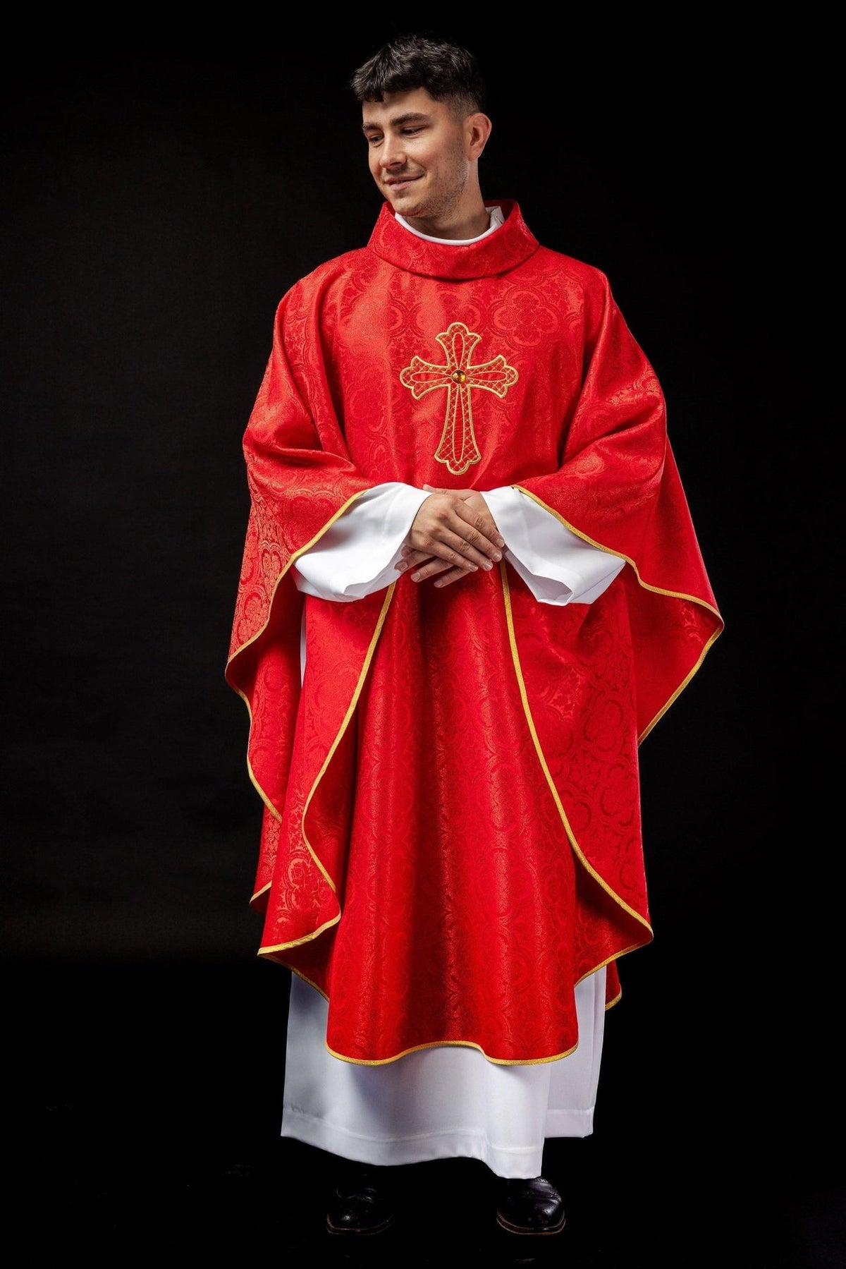 Red chasuble worn front view with gold trim, patterned fabric and cross embroidery