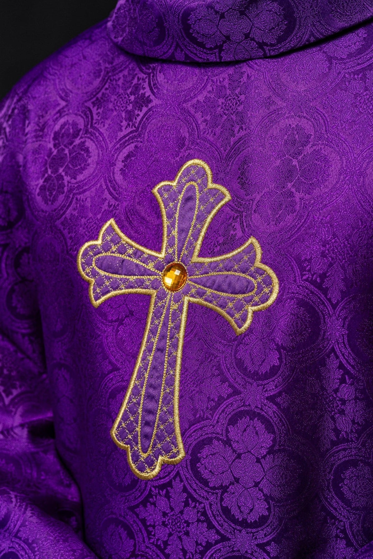 Purple chasuble close-up showing gold cross embroidery and patterned fabric