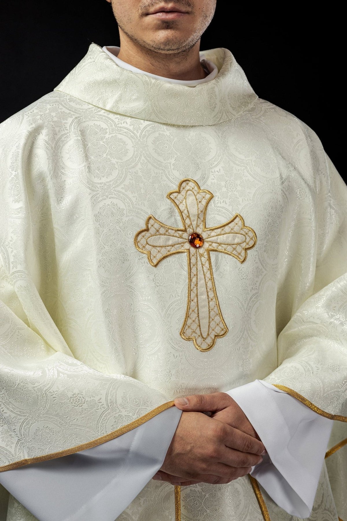 Ecru chasuble close-up showing embroidered gold cross and patterned fabric
