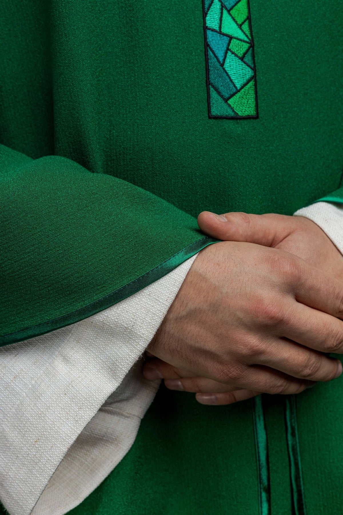 Green chasuble close-up showing green polyester fabric and trim edge