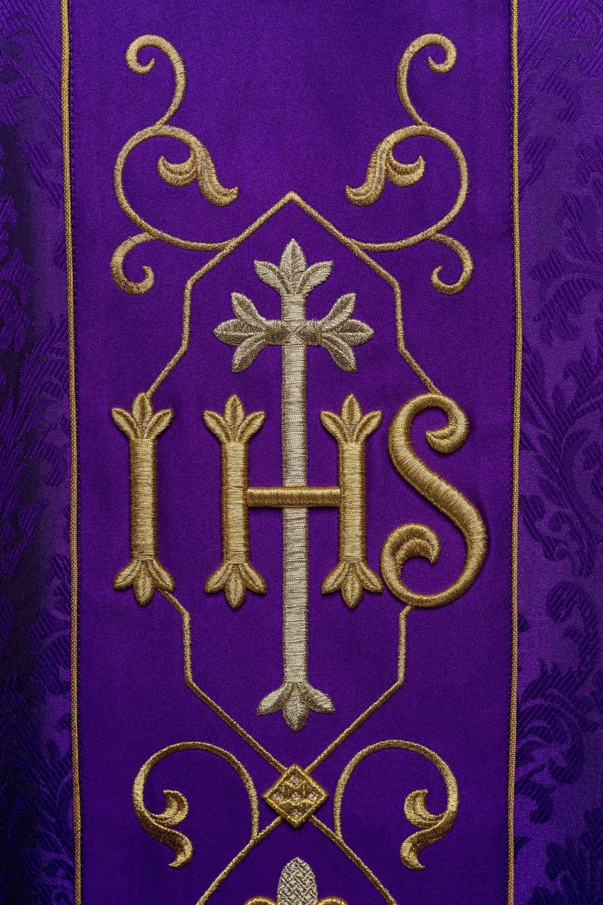 Purple chasuble close-up showing embroidered IHS, cross and gold scrollwork