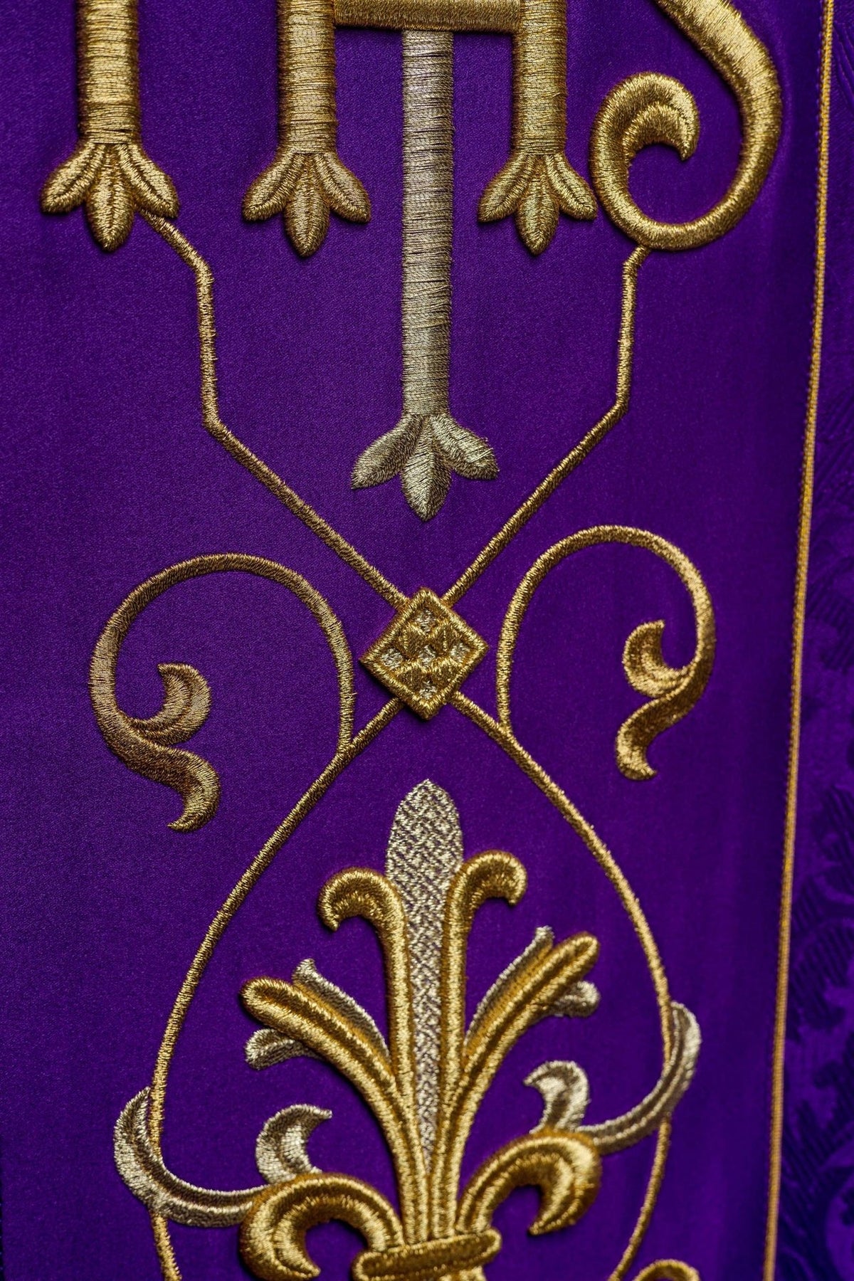 Purple chasuble embroidery close-up with gold scrollwork and decorative floral motif