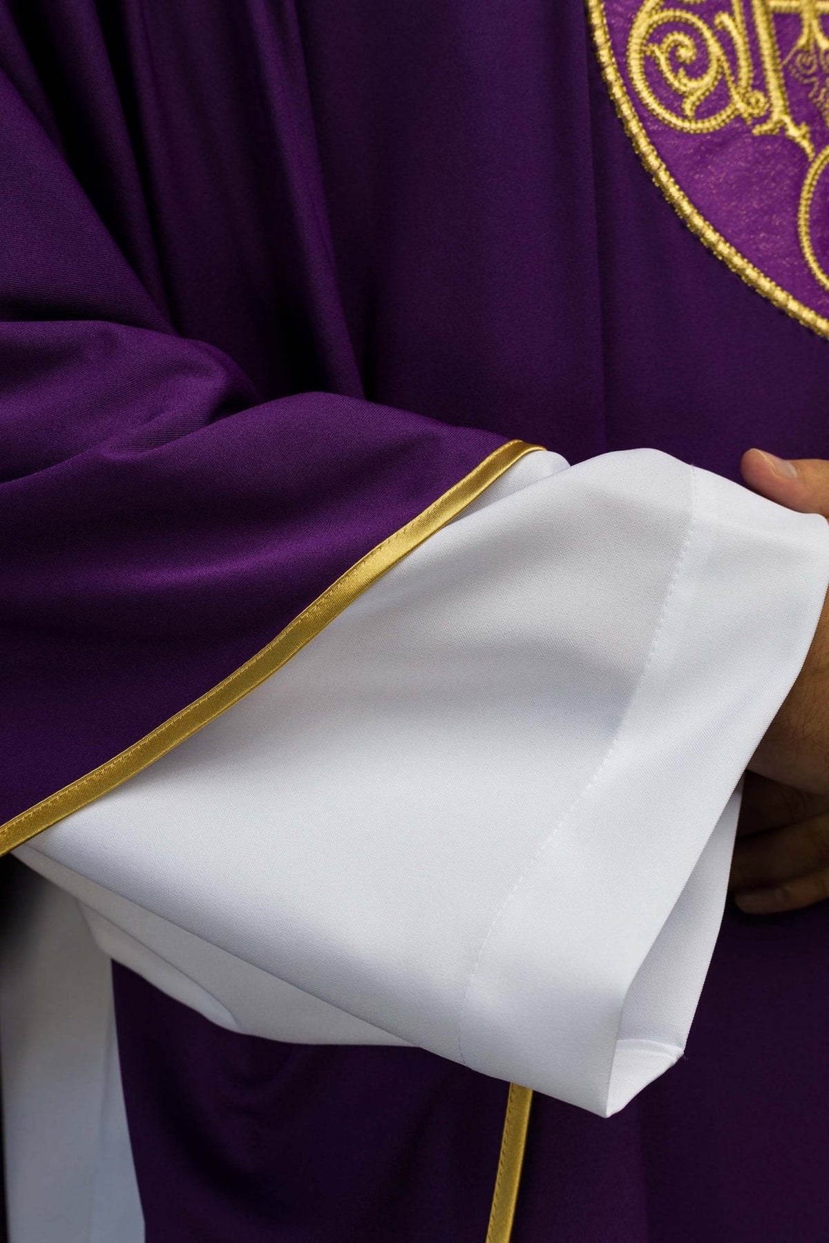 Purple chasuble close-up showing white sleeve cuffs and gold trim