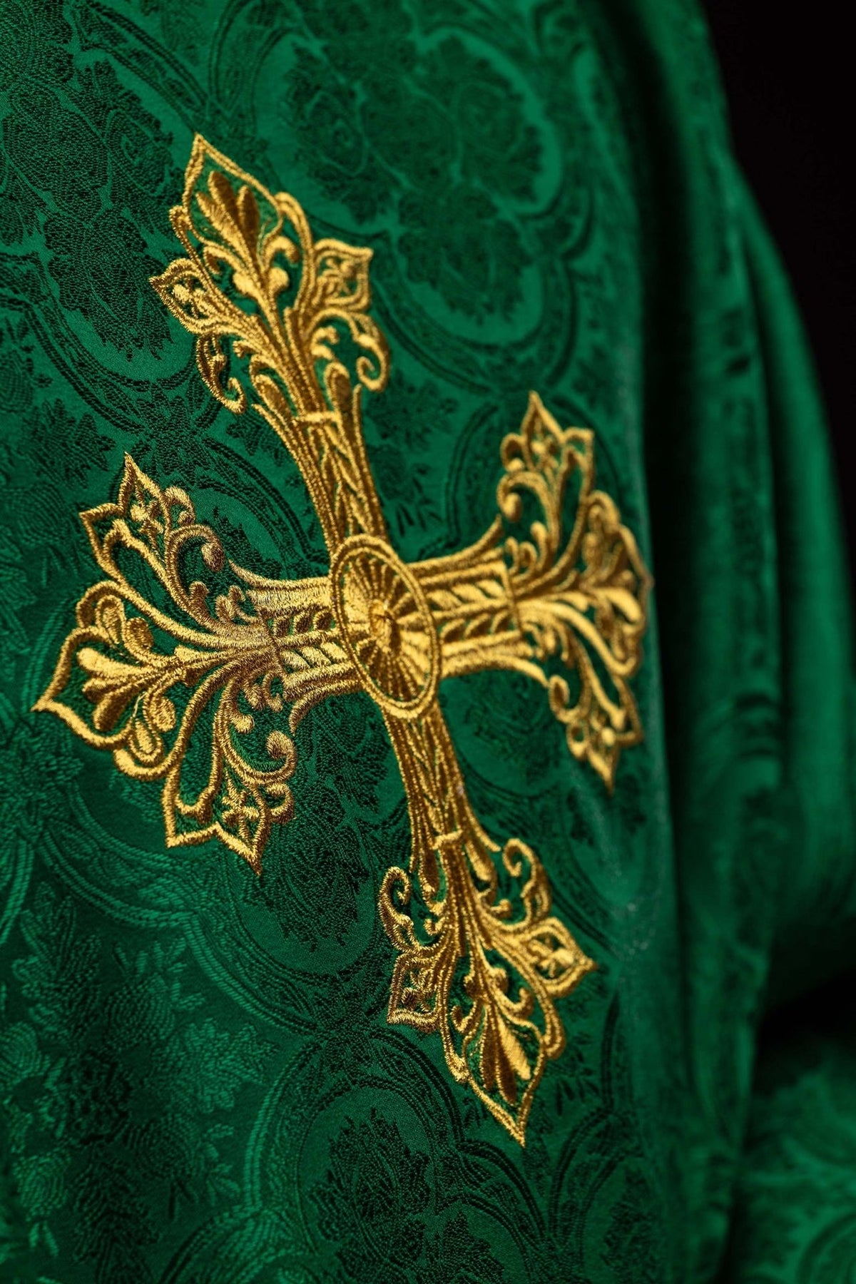 Green chasuble close-up showing embroidered gold cross on jacquard fabric