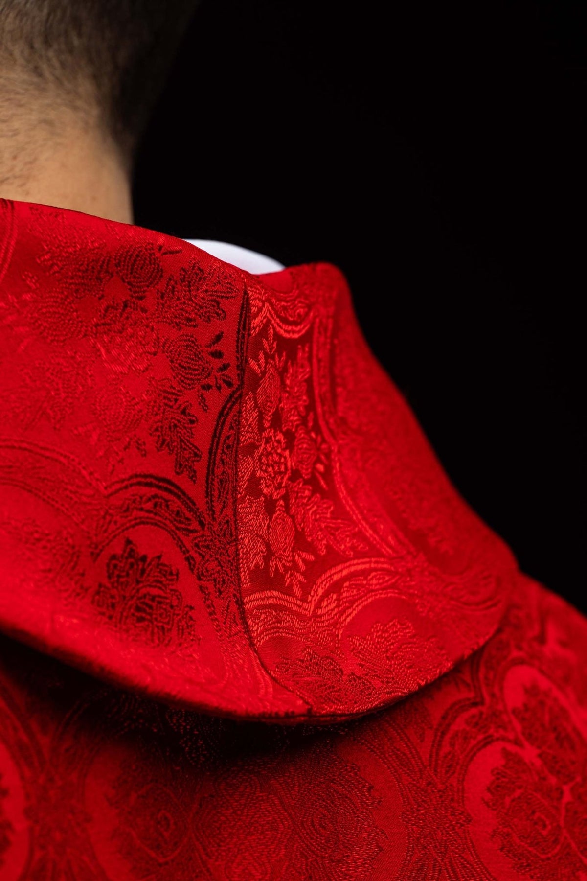 Red chasuble close-up showing patterned jacquard fabric and stand-up collar