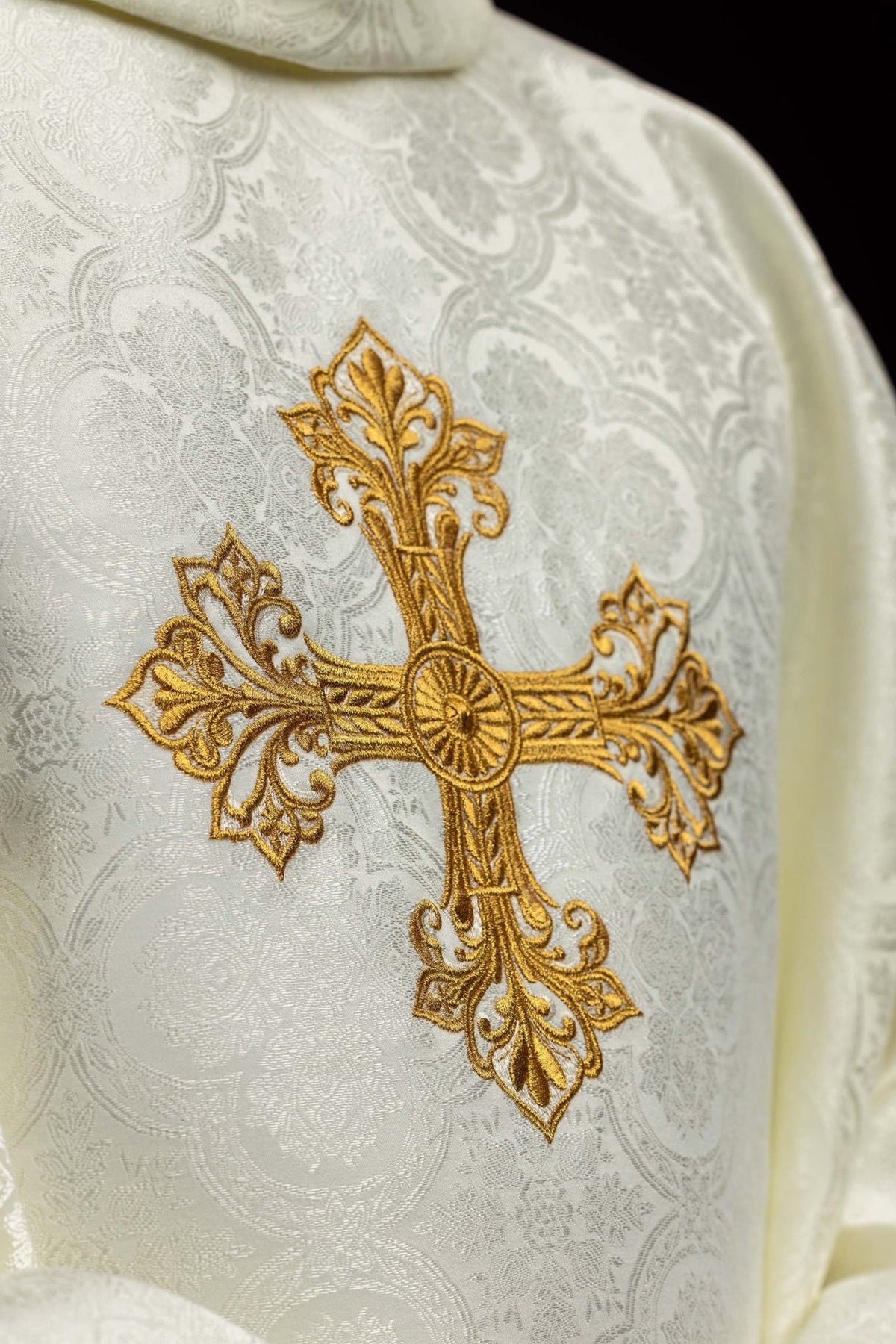Ecru chasuble close-up showing ornate gold embroidered cross