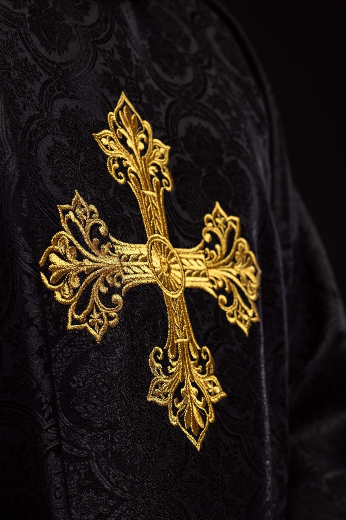 Black chasuble close-up of ornate gold embroidered cross on jacquard fabric