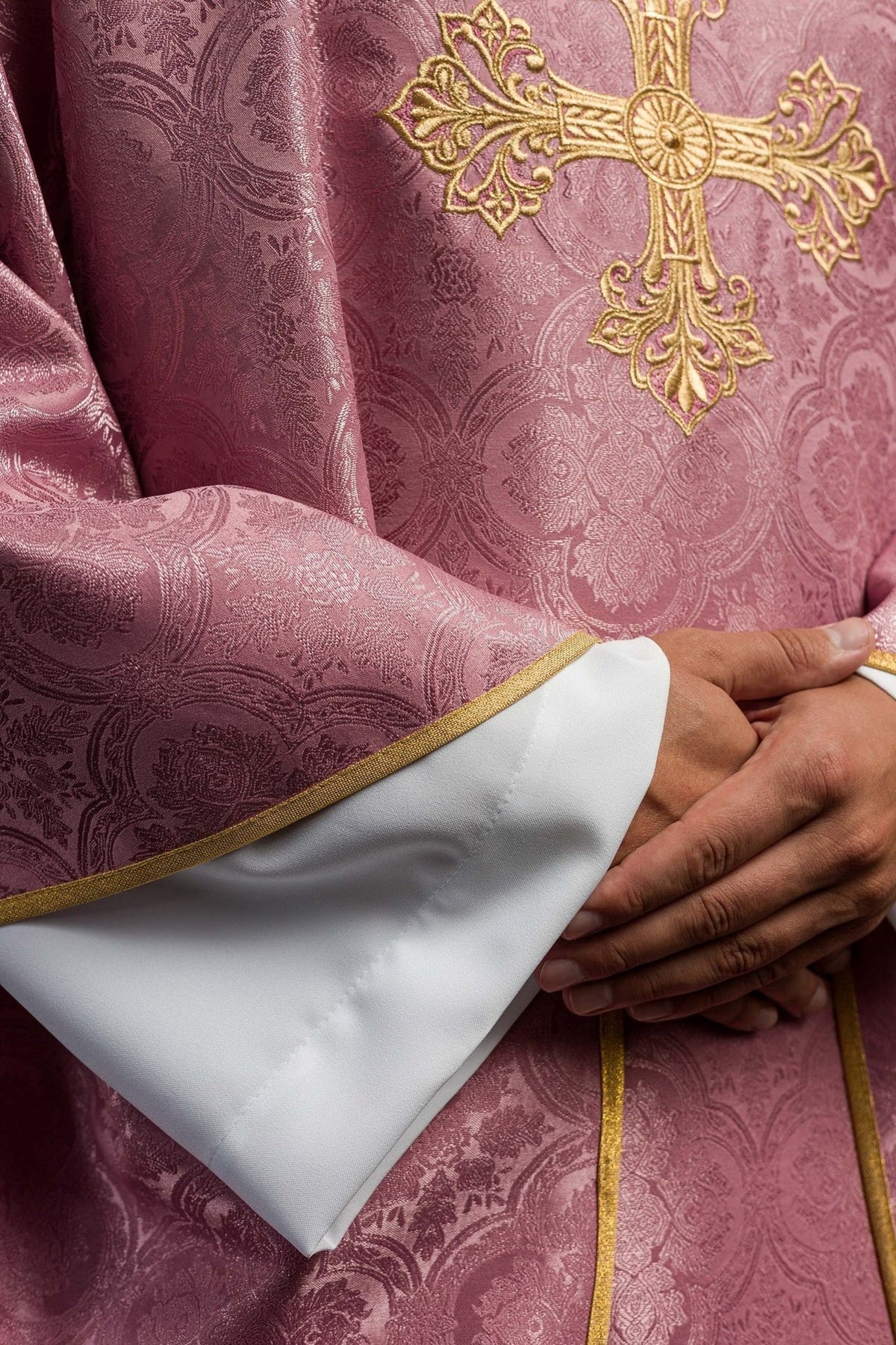Rose chasuble detail showing patterned fabric, gold trim and white sleeve opening