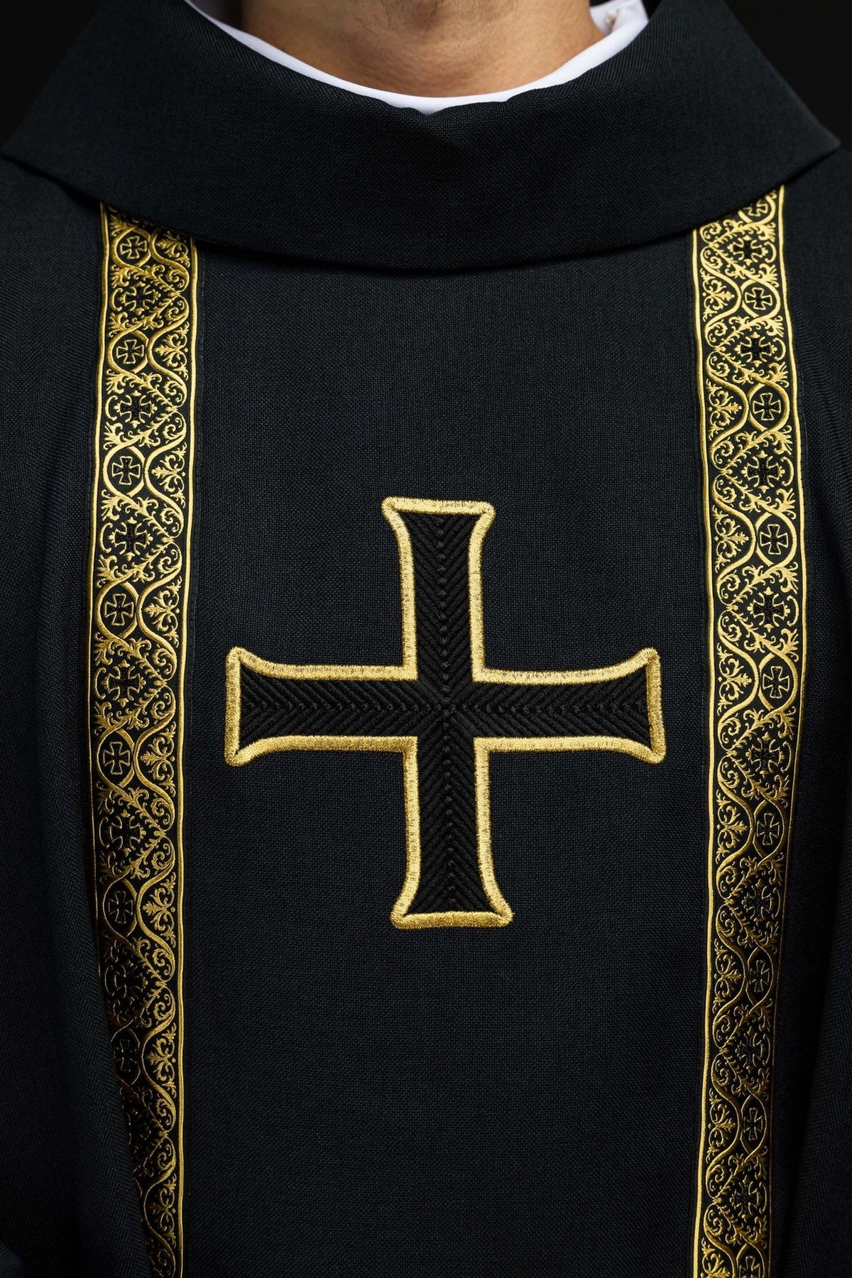 Black chasuble close-up showing gold cross embroidery and patterned orphreys