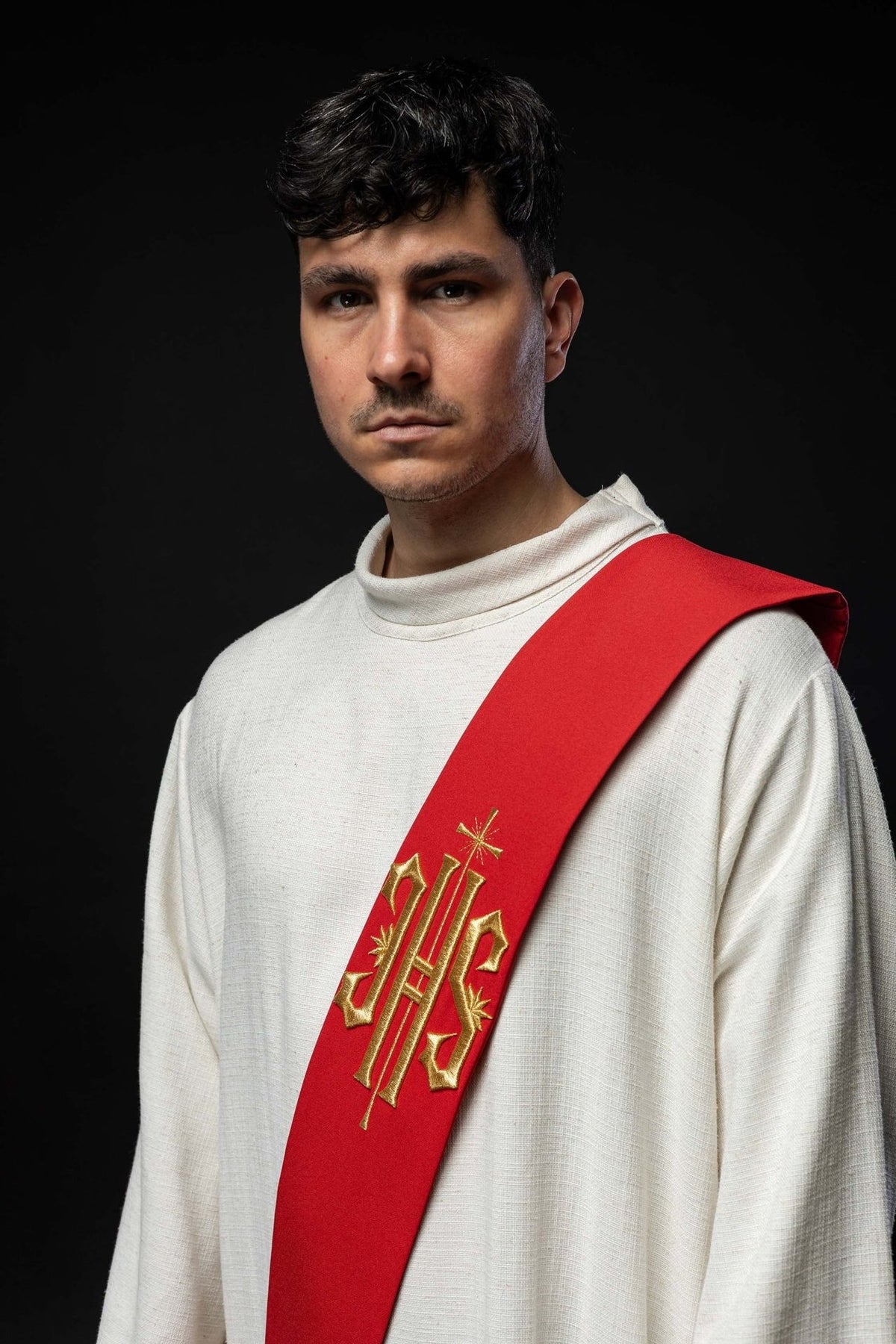 Red embroidered stole worn in a close front view with gold IHS and cross