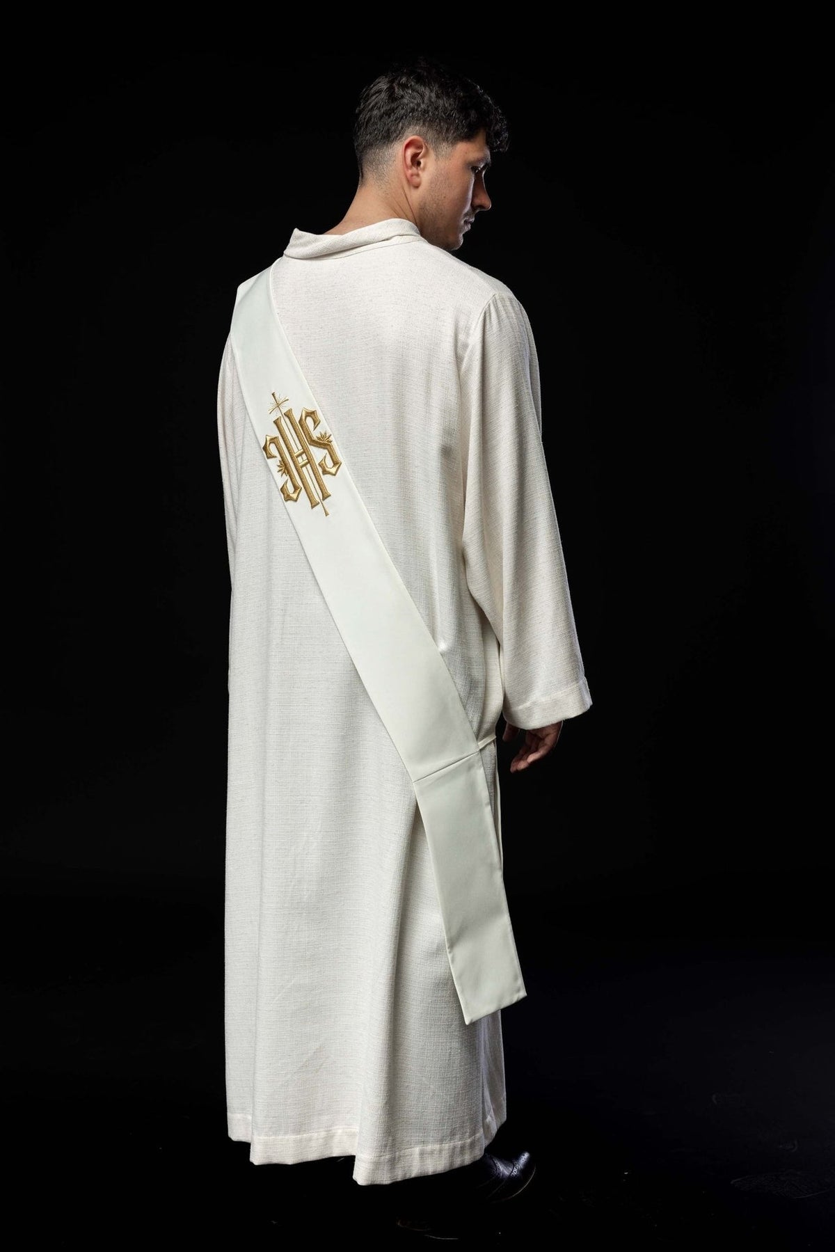 Side view of white stole worn over a liturgical garment, with gold embroidered IHS