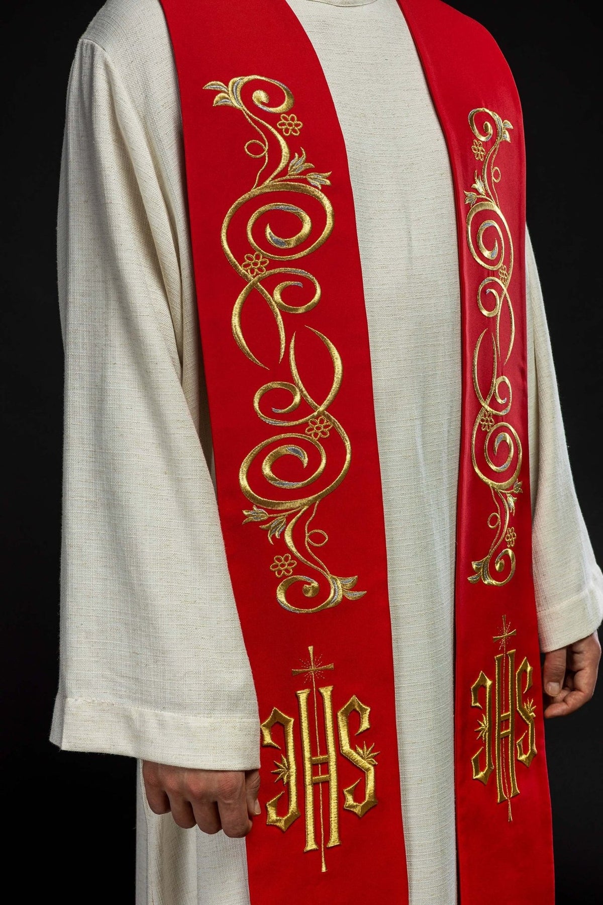 Red stole close-up showing embroidered gold floral scrollwork and IHS symbols