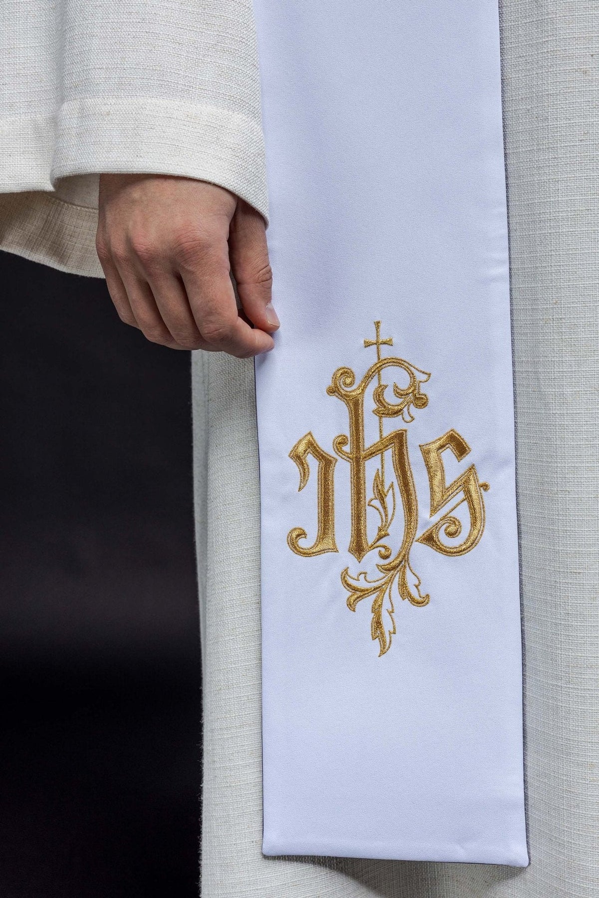 White stole close-up showing detailed gold IHS embroidery