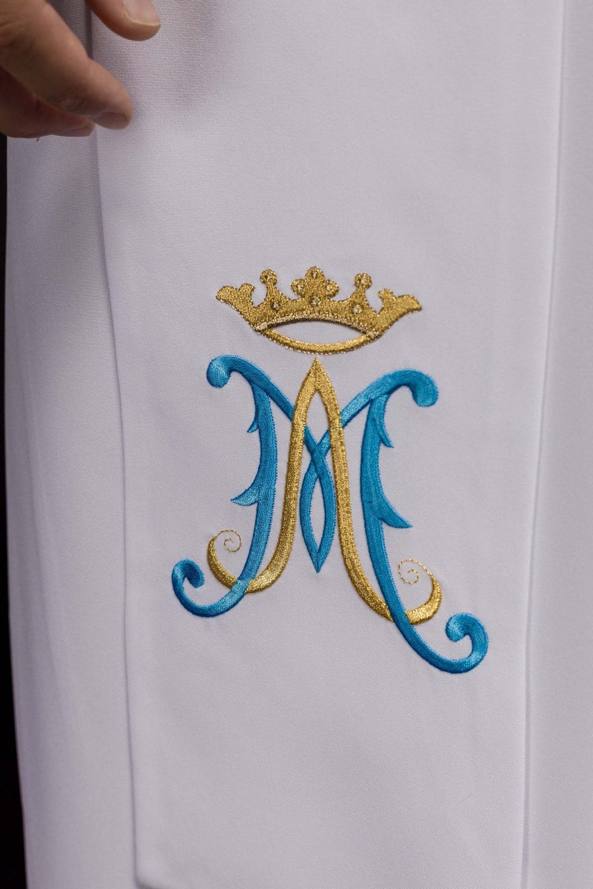 Embroidered stole detail showing a blue and gold Marian symbol on white fabric
