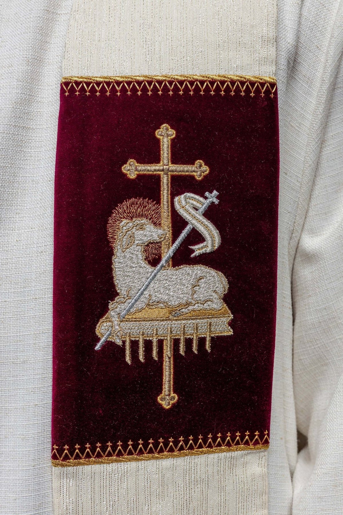 Stole close-up showing the embroidered Agnus Dei symbol with cross on a burgundy panel