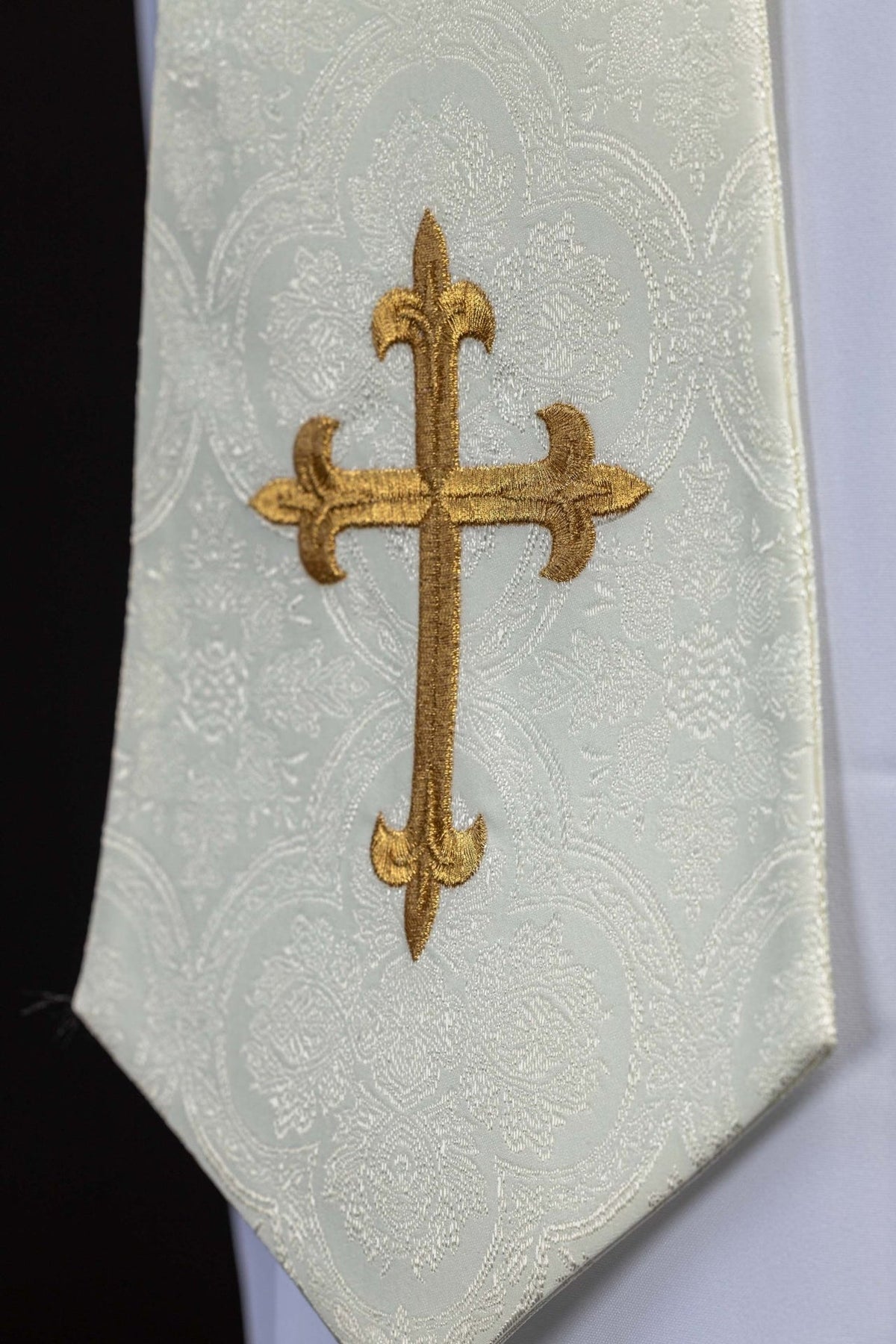 Ecru stole close-up showing embroidered gold cross and jacquard pattern