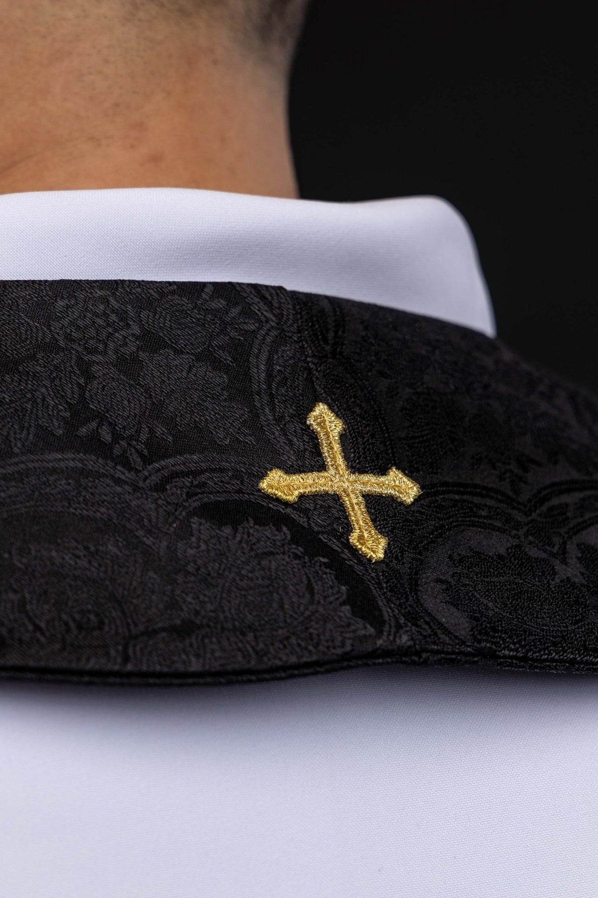 Black stole close-up showing gold embroidered cross and jacquard fabric