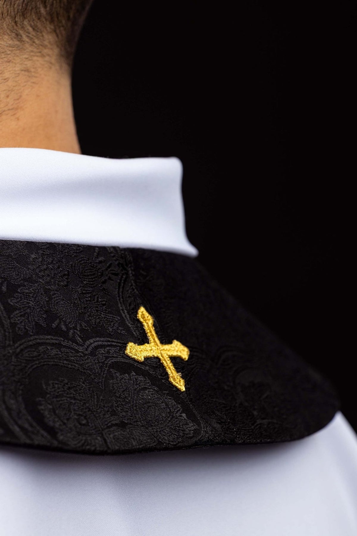 Black stole close-up showing embroidered gold cross at the collar
