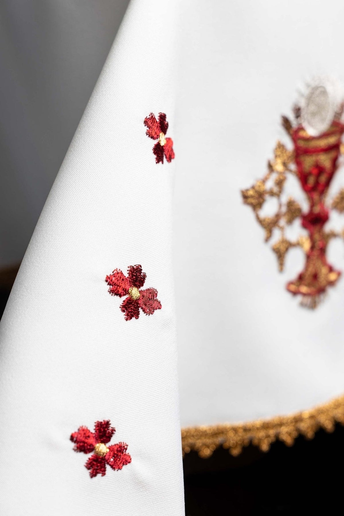 White chalice veil detail with embroidered red floral motifs and gold trim