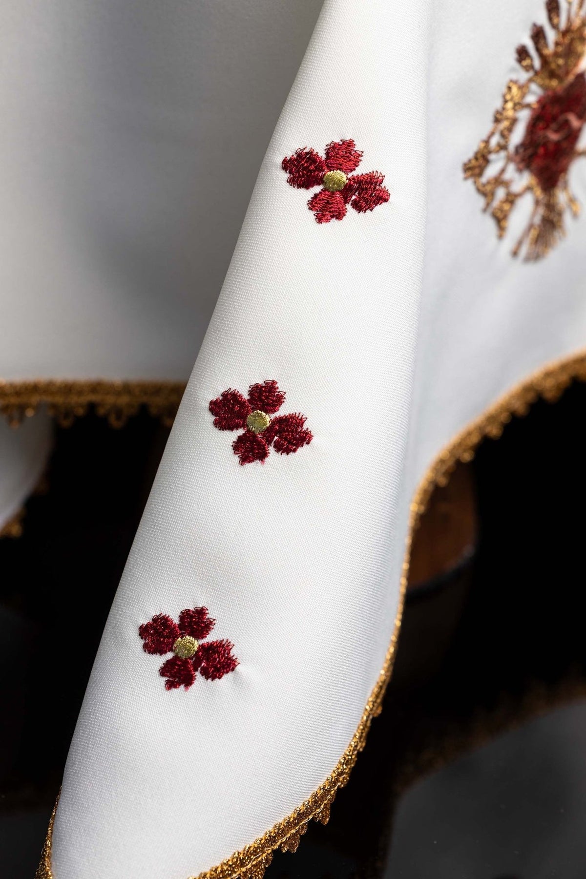 White chalice veil detail with repeated red floral embroidery and gold edging