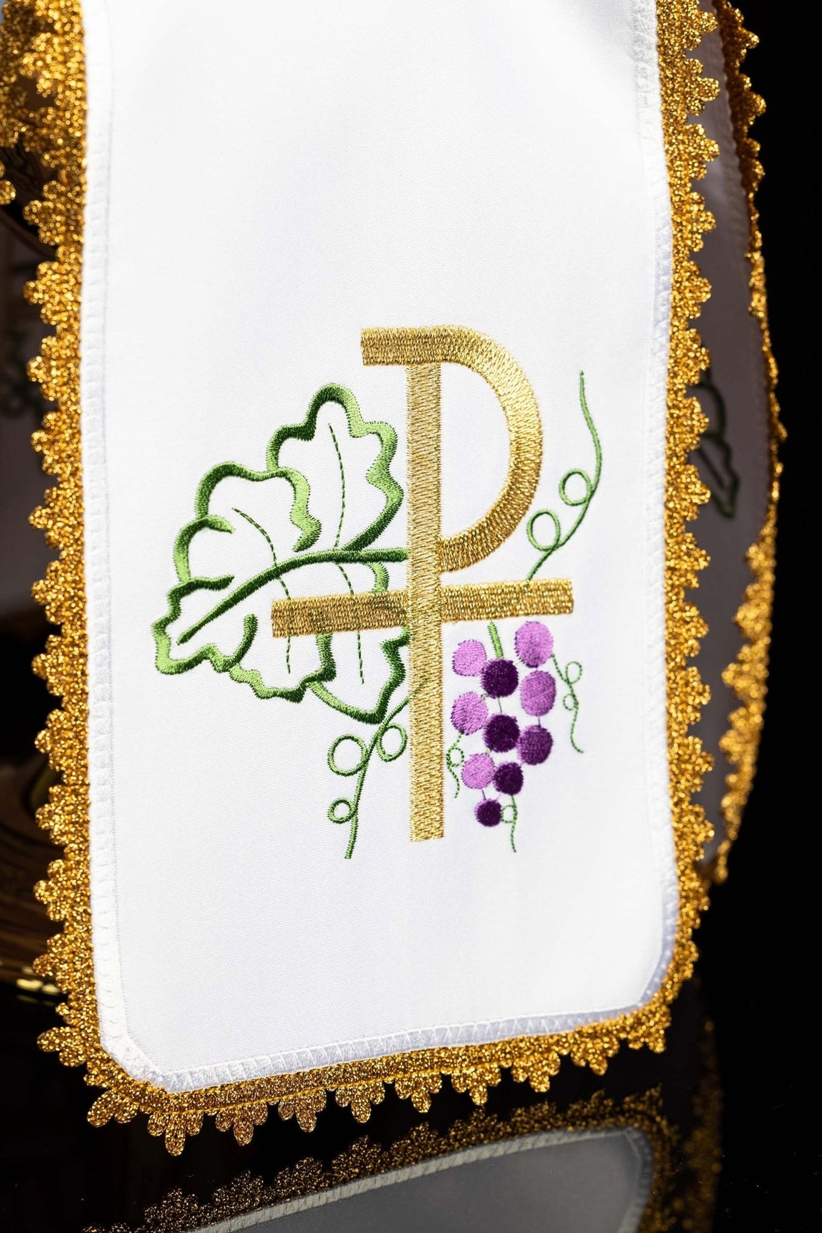 Ciborium veil close-up showing white fabric, gold cross embroidery, green vine and purple grapes
