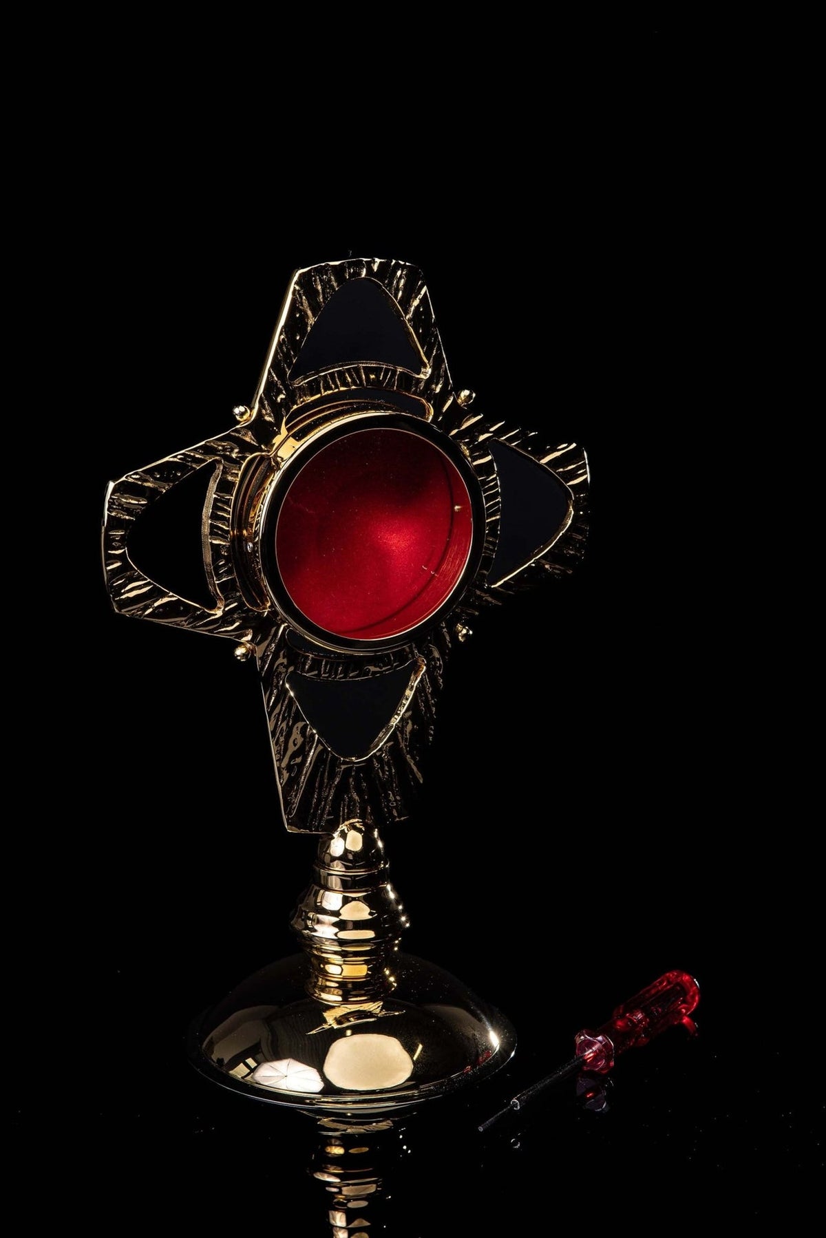 Brass reliquary front view with red circular center and textured gold rays