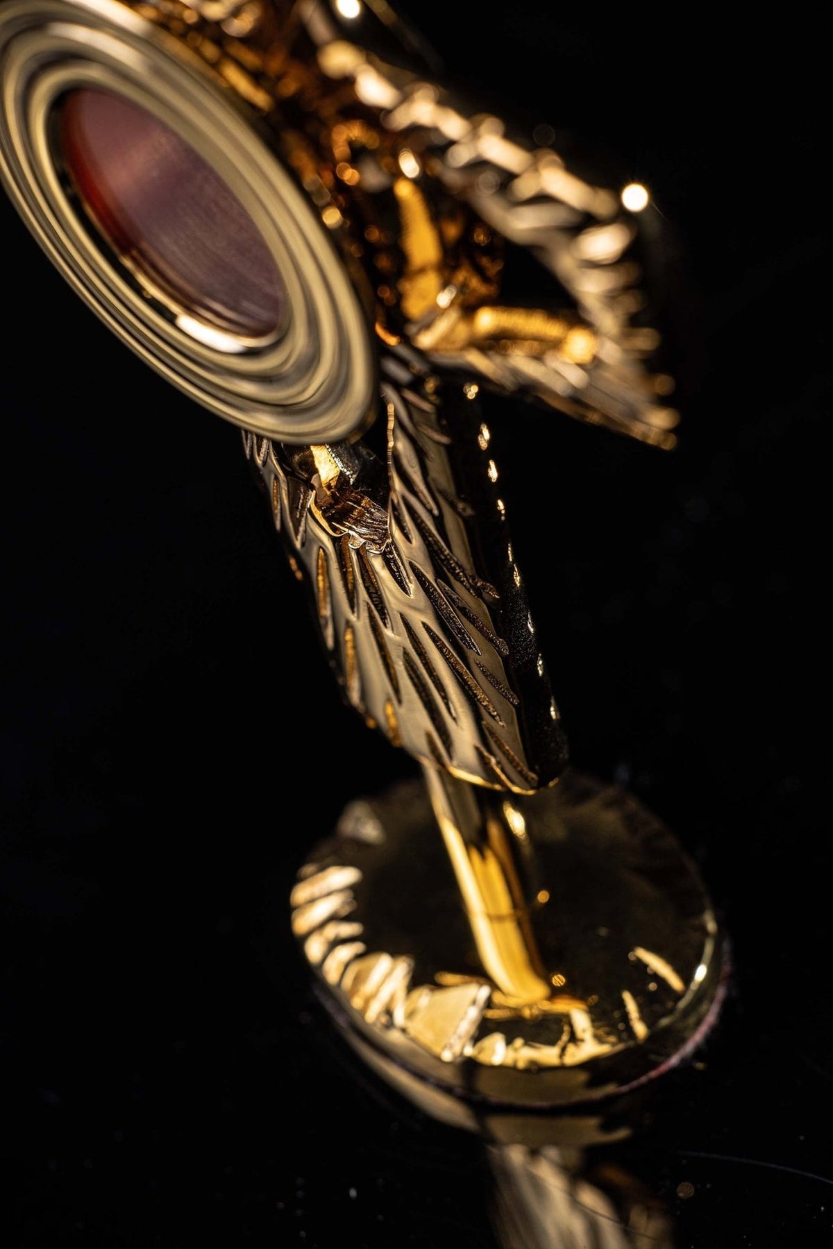 Gilded brass reliquary detail showing circular red center, textured cross and pedestal