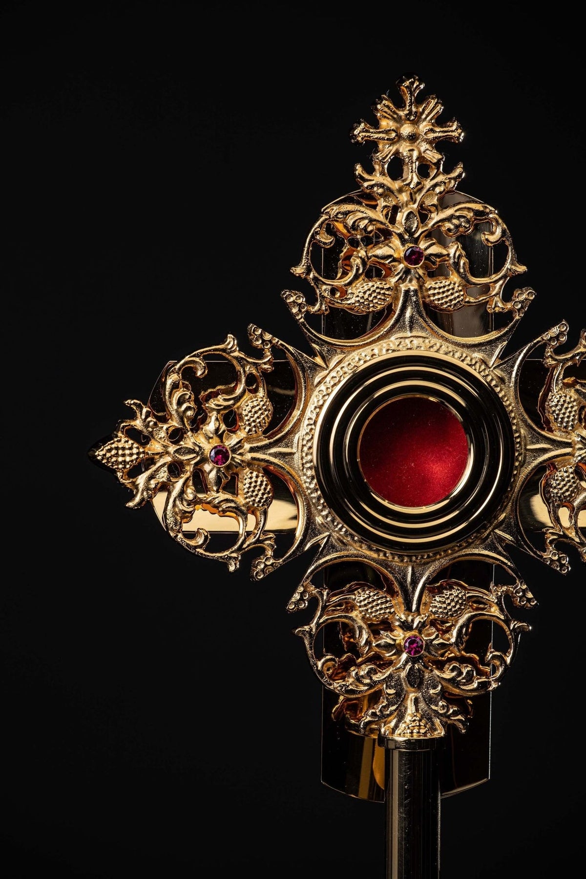 Brass reliquary close-up showing red center, ornate scrollwork, cross, and red stones