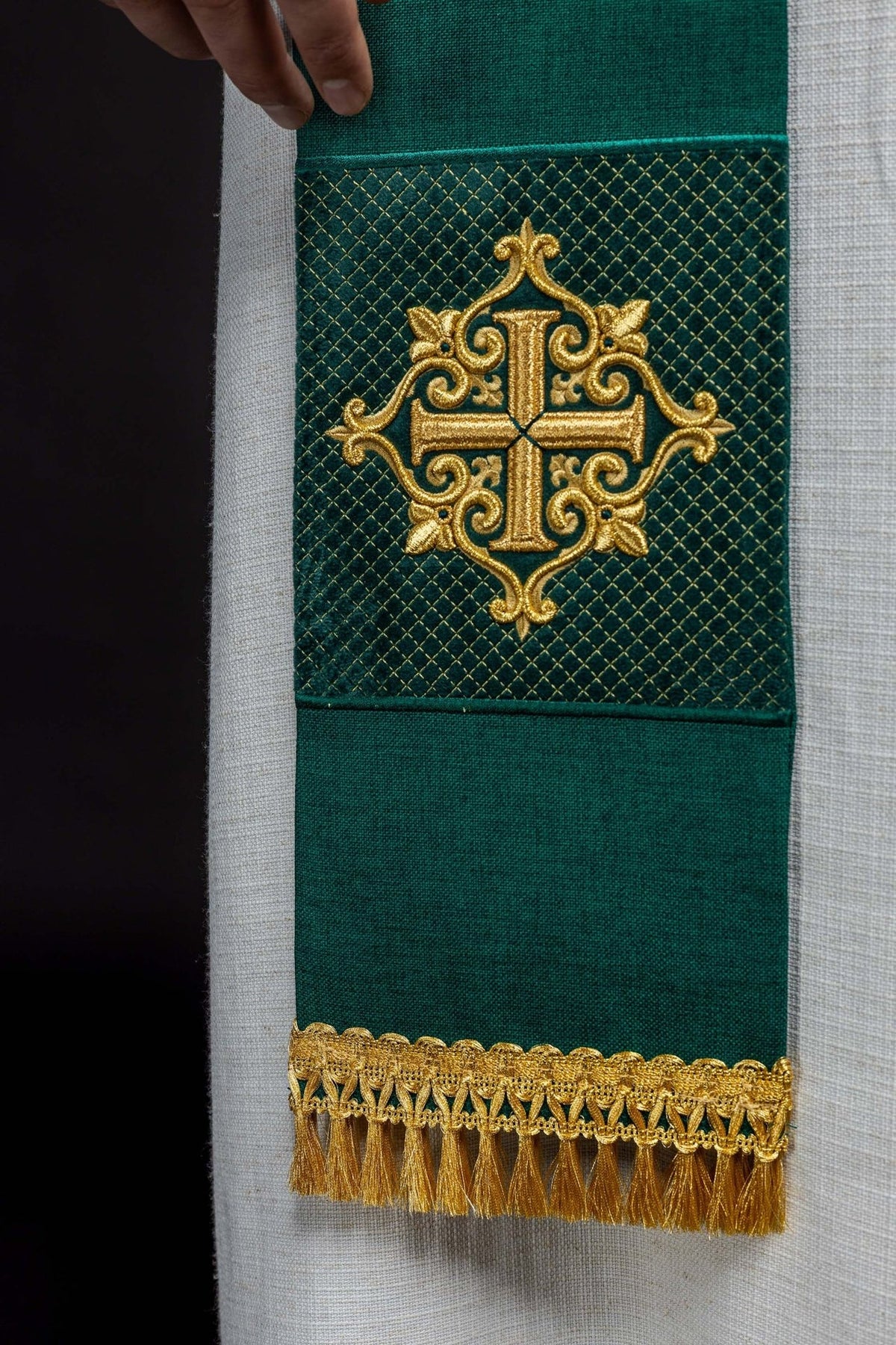 Green velvet stole close-up showing embroidered gold cross and fringe