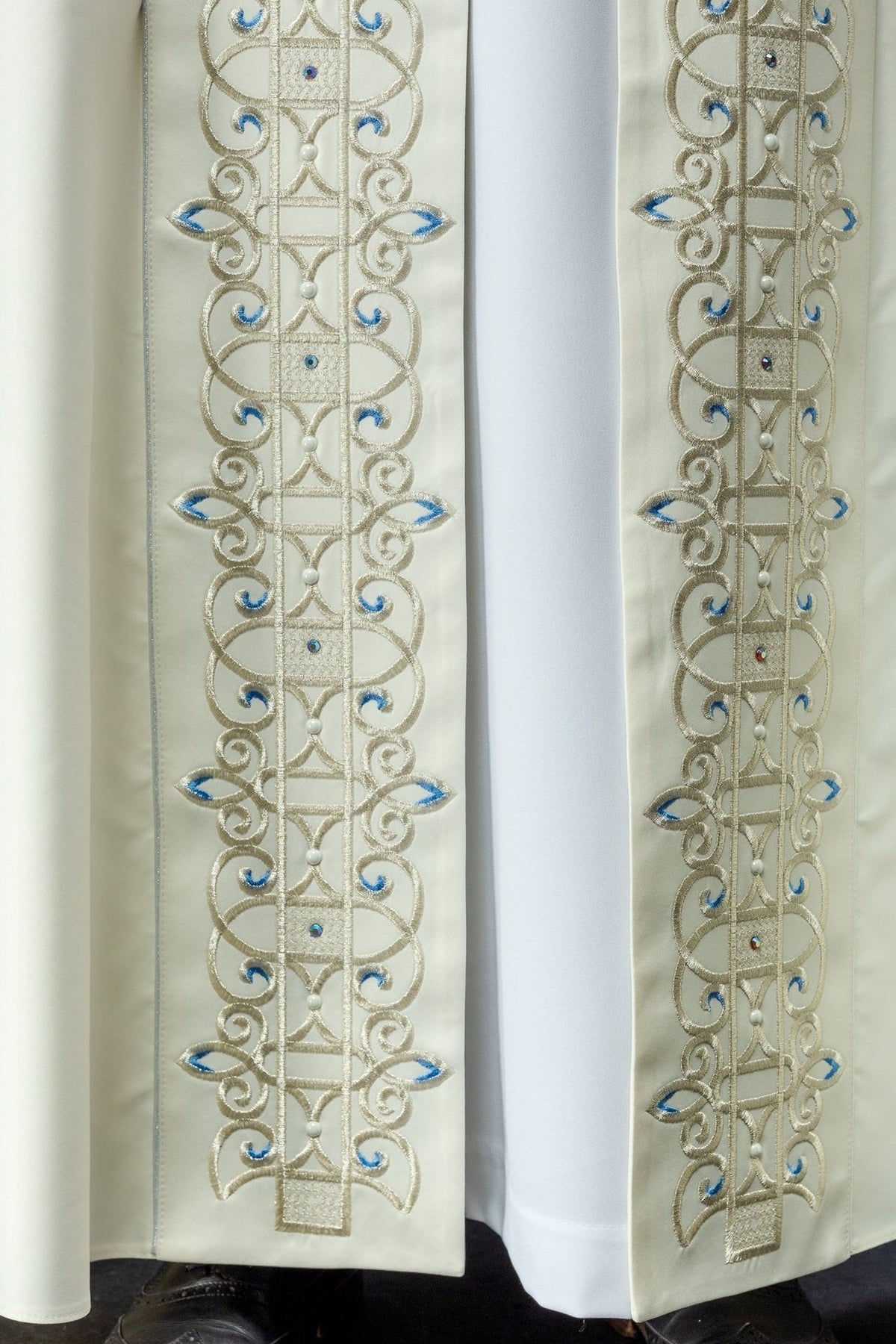 Ivory cope front embroidery close-up with repeating gold and blue motifs
