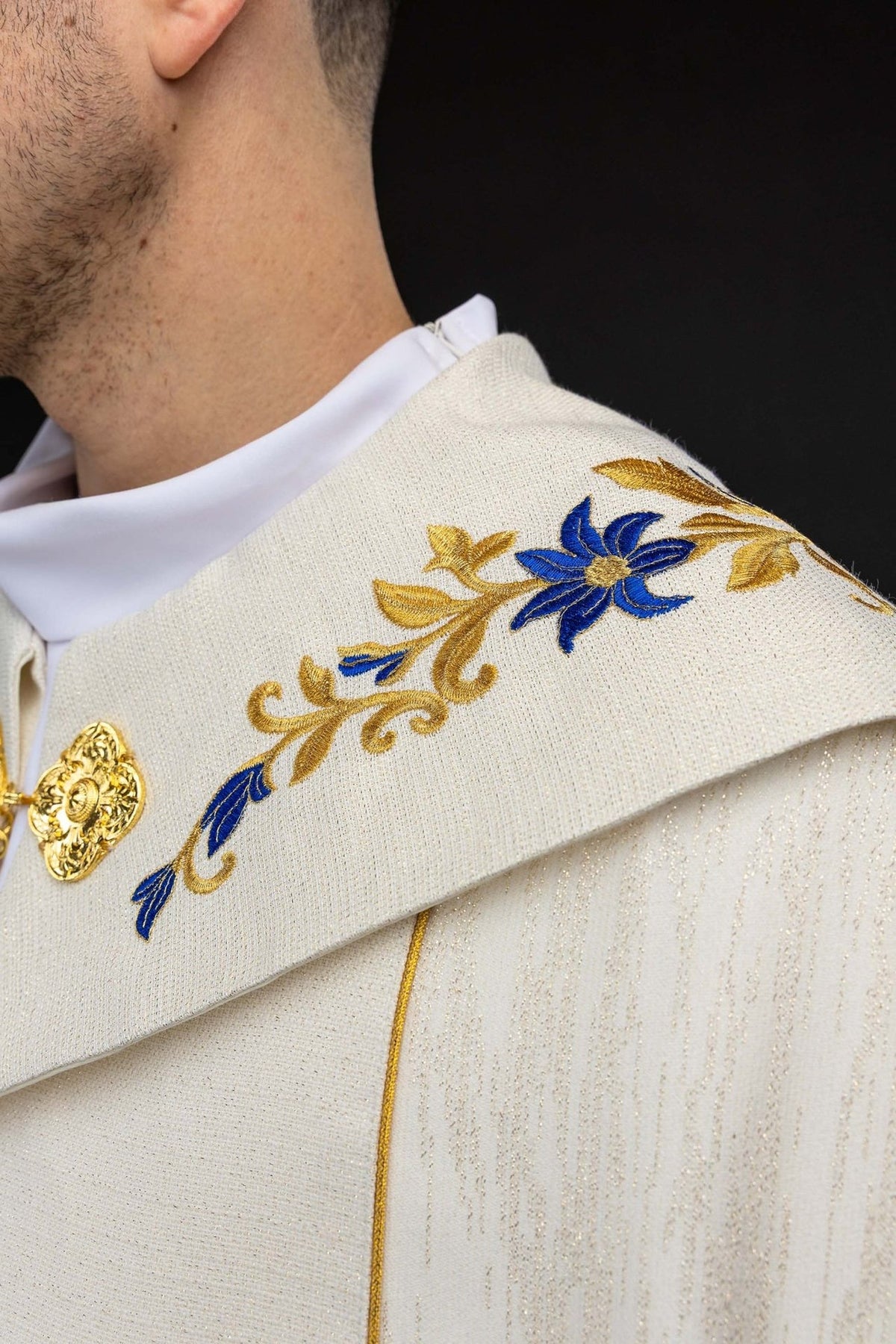 Ecru cope close-up of gold clasp and blue and gold embroidered trim