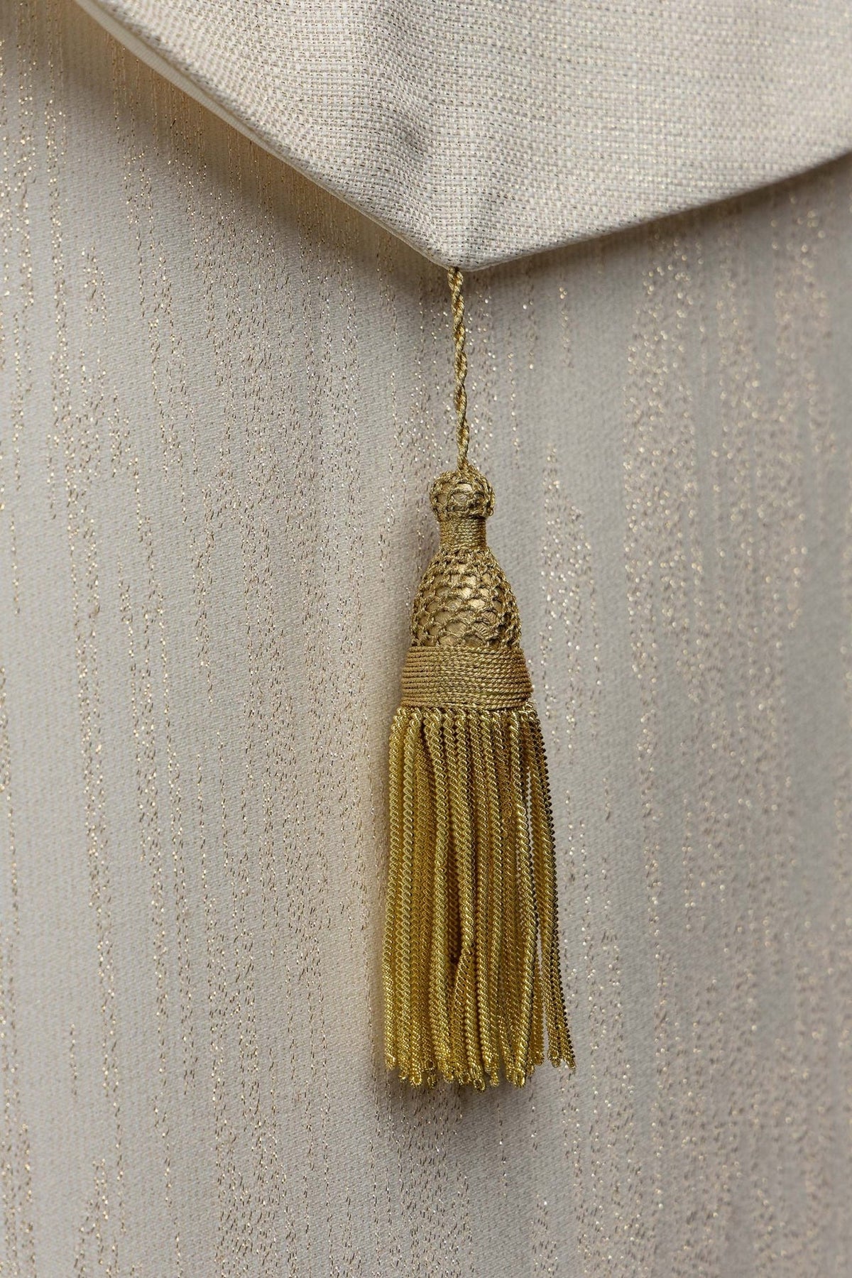 Ecru cope close-up of gold tassel and textured fabric