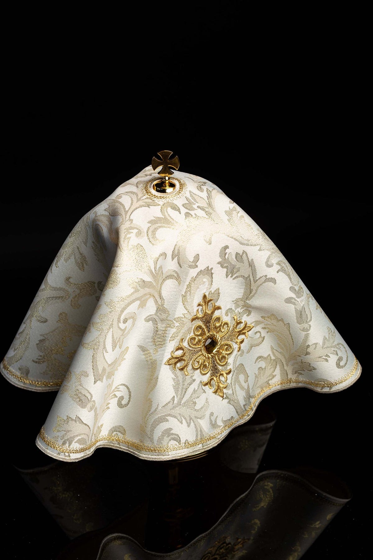 Ciborium veil angled view showing ecru fabric, gold cross embroidery, stone, and trim