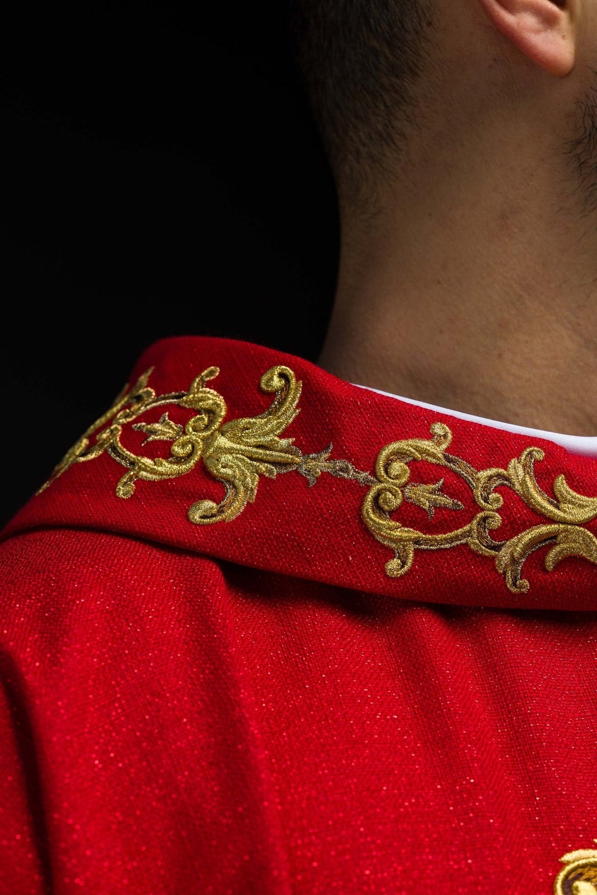 Red chasuble close-up showing gold embroidered cross with a central stone