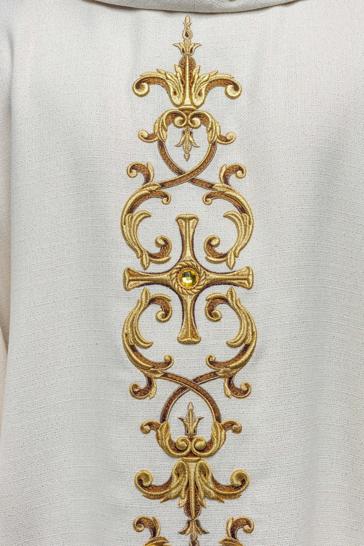 Catholic chasuble, close-up of white fabric and gold embroidery with a central stone