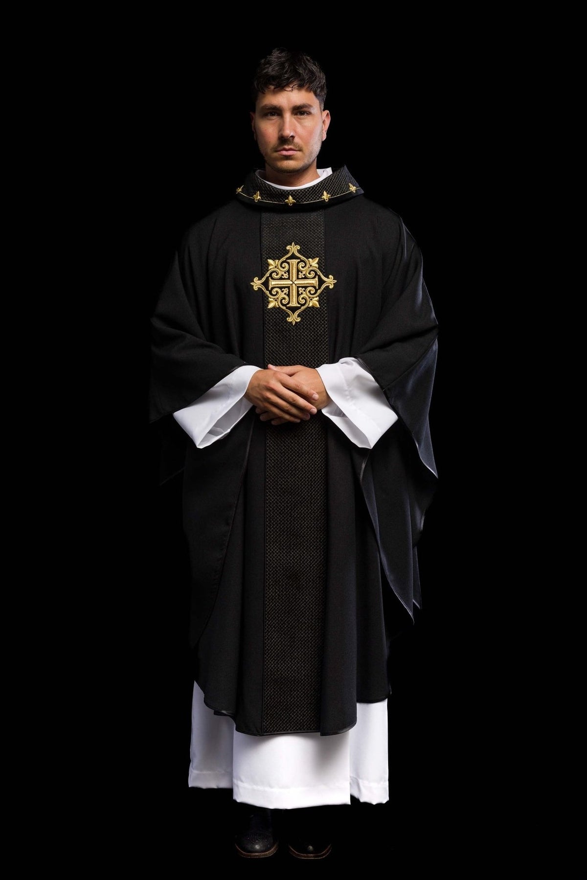 Black velvet chasuble worn in front view, showing gold cross embroidery and wide sleeves
