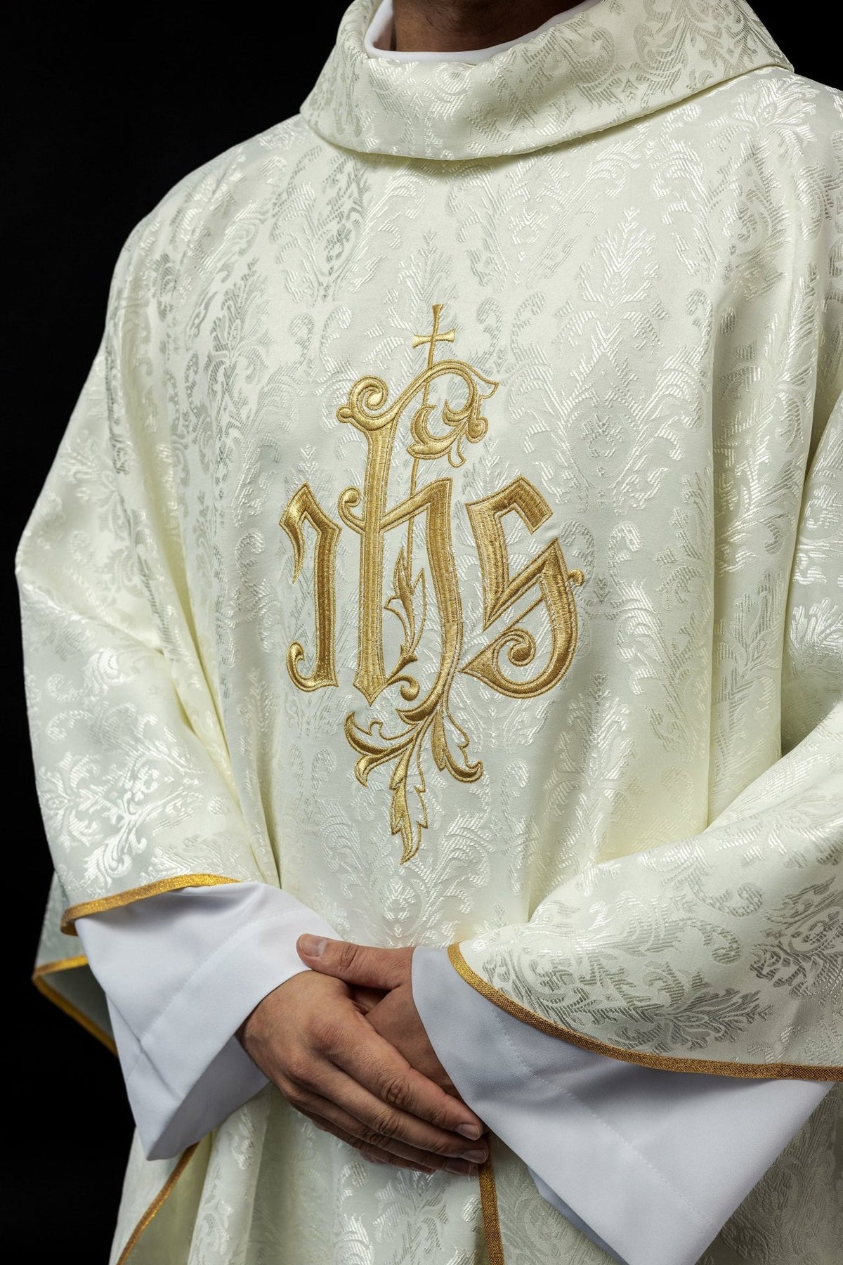 Ecru chasuble close-up showing gold IHS embroidery and decorative fabric