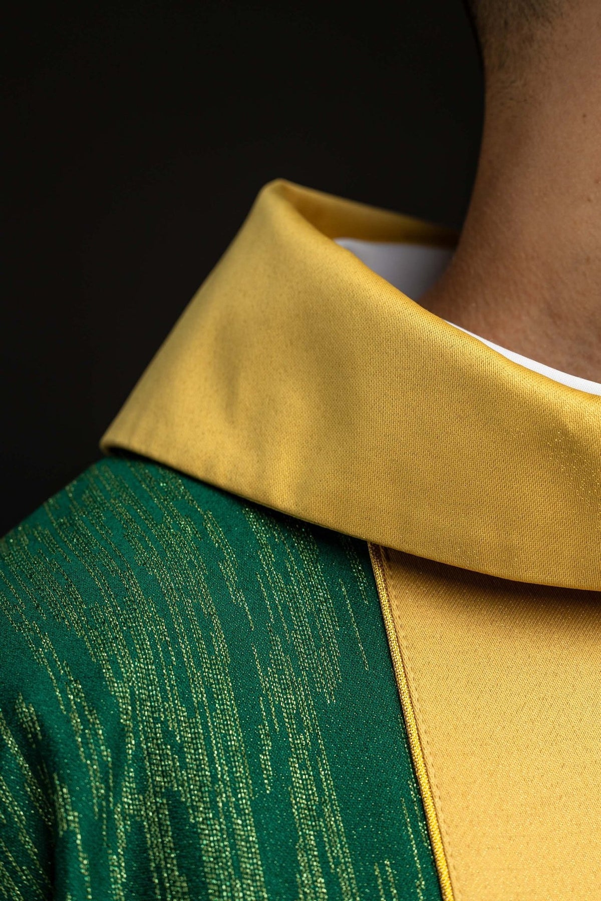 Green chasuble detail showing gold sleeve trim and embroidered cross