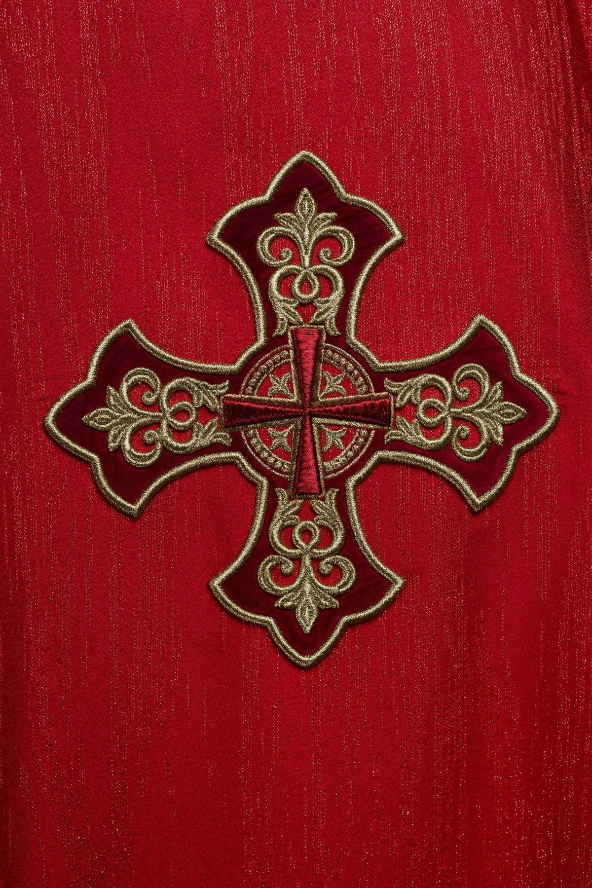 Red chasuble close-up showing embroidered gold cross motif on decorative fabric