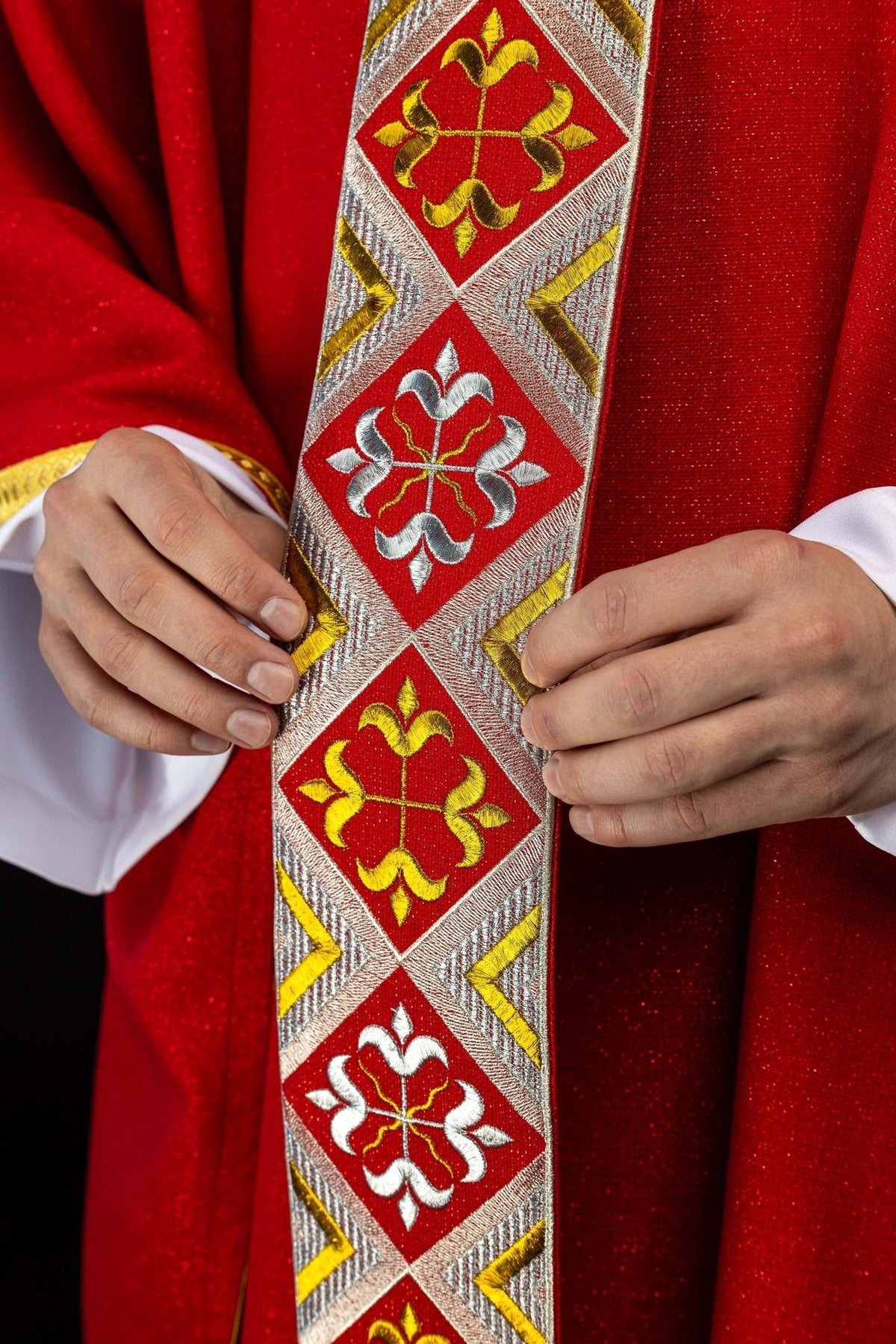 Red chasuble close-up showing gold embroidered trim and white sleeve