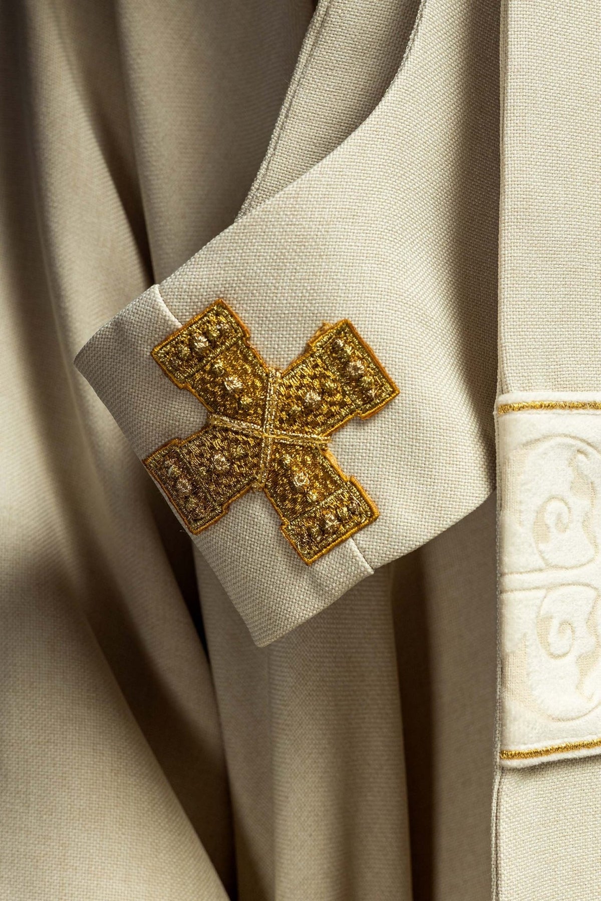 Ecru chasuble close-up of an embroidered gold cross on the sleeve orphrey