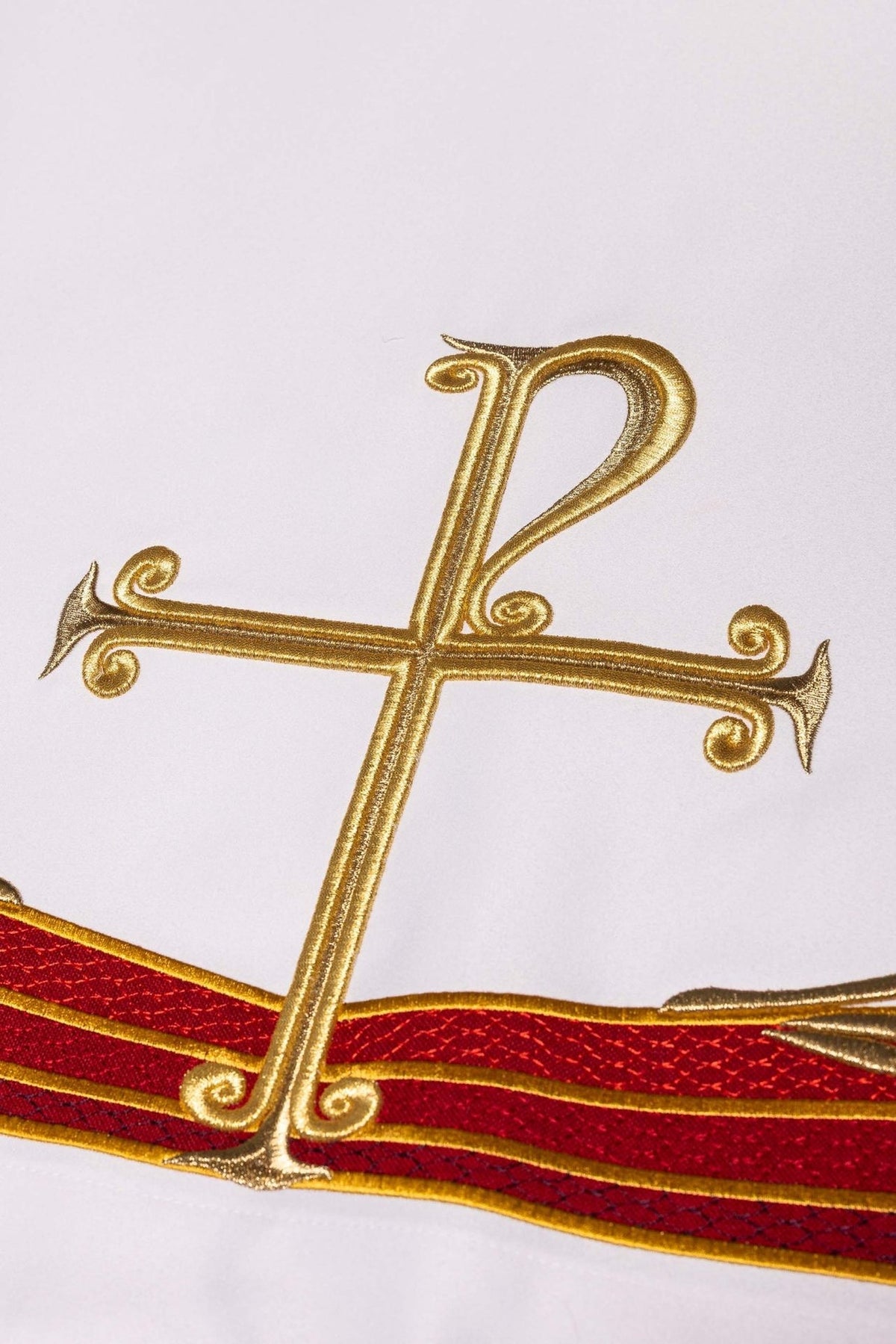 White altar cloth close-up showing gold PAX cross and red embroidered bands