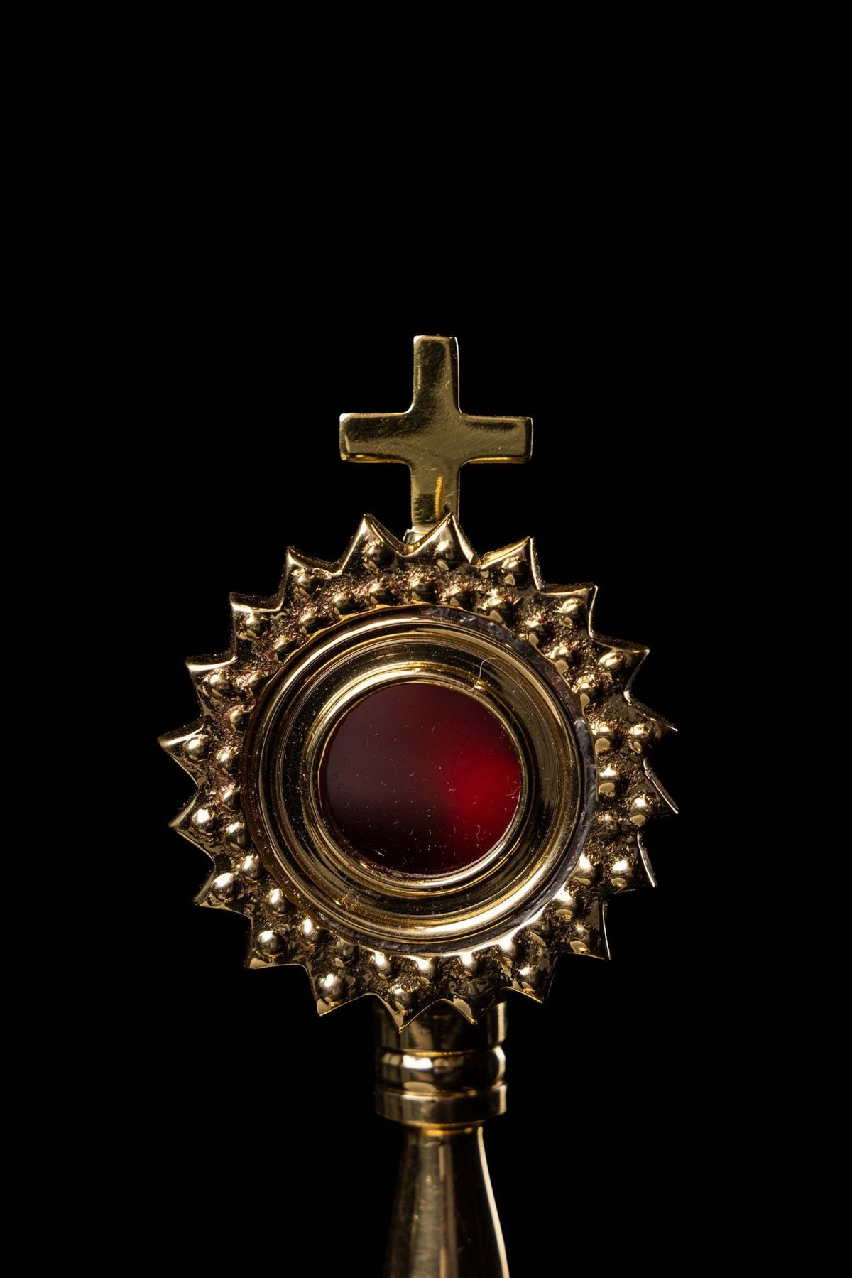 Brass reliquary close-up, front view showing red center, radiant motif, and cross