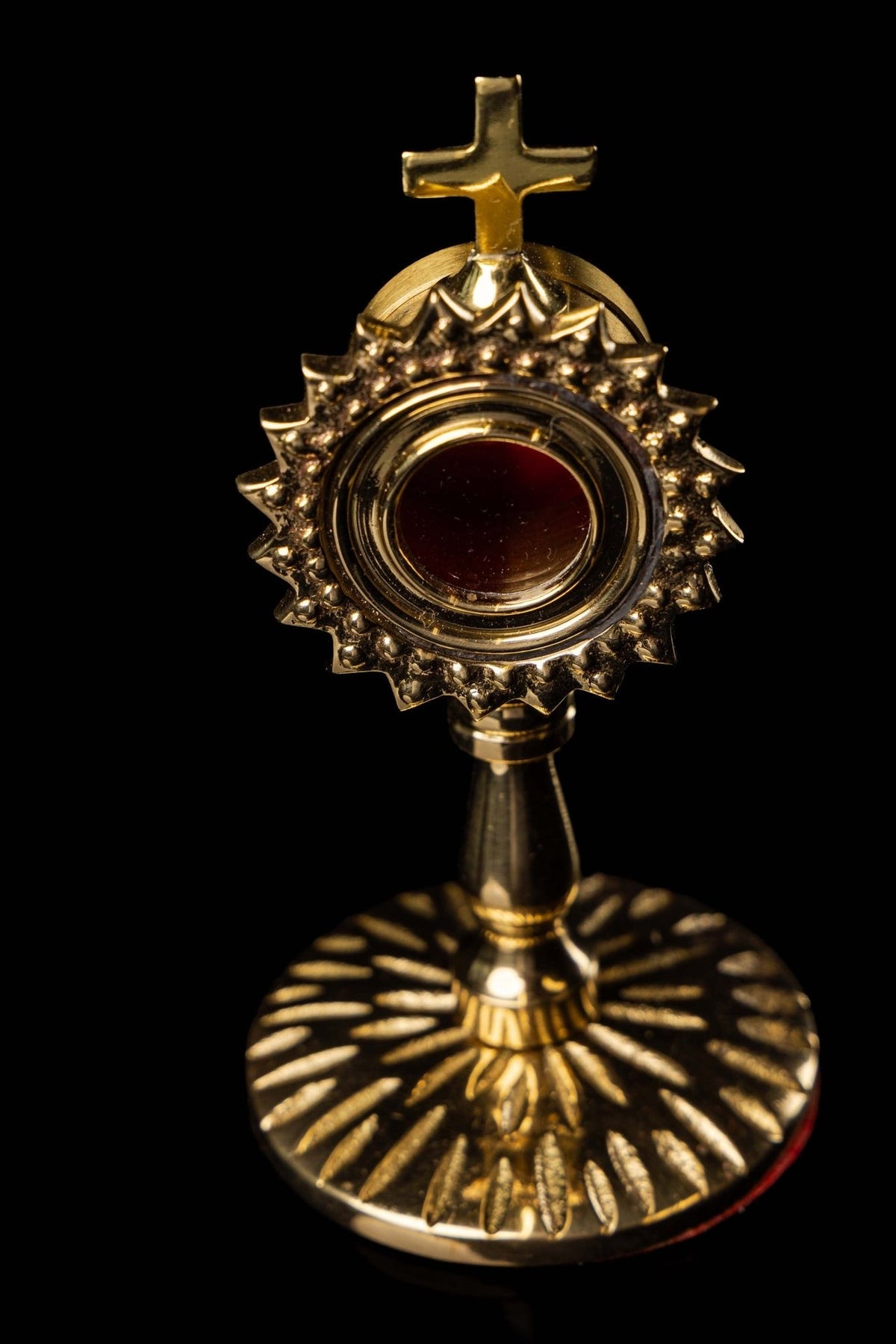 Brass reliquary angled view showing the cross, red center, stem, and radiant base