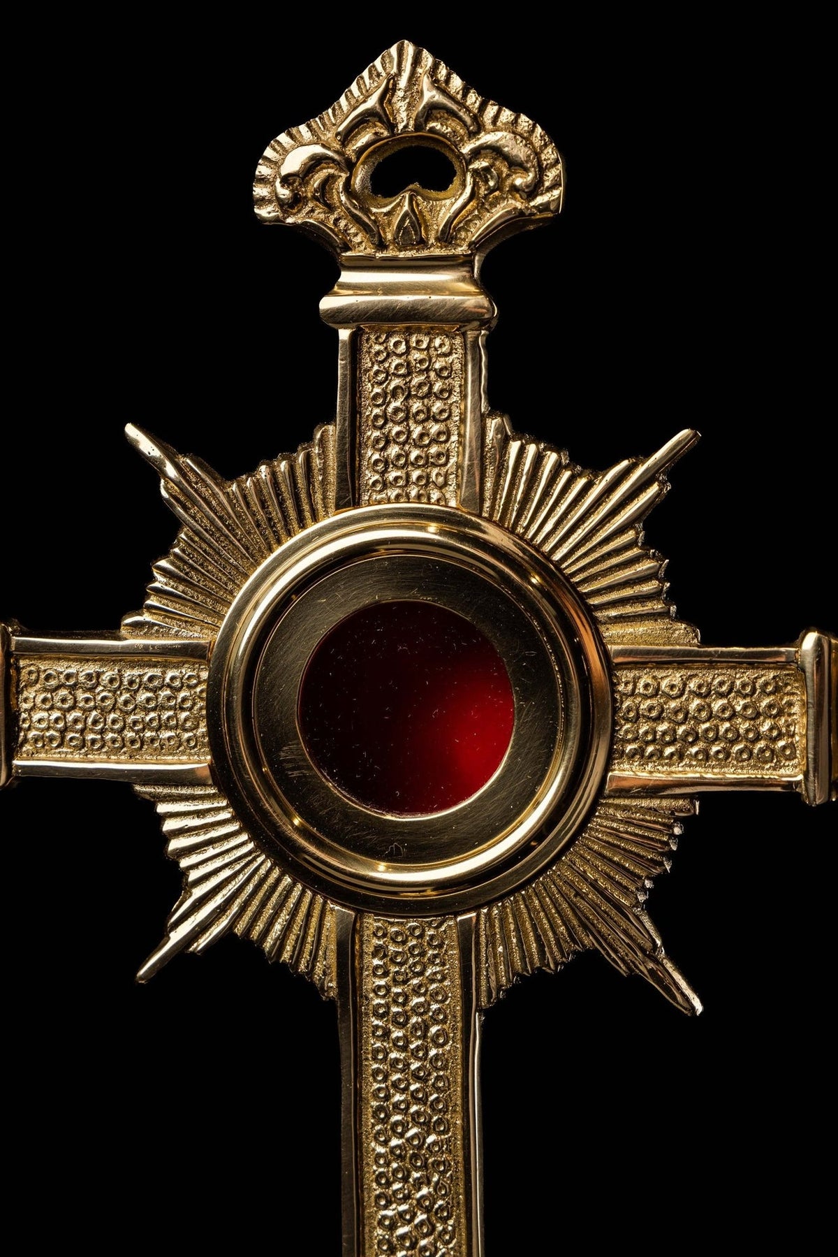 Brass cross reliquary close-up showing ornate top, textured arms and red center
