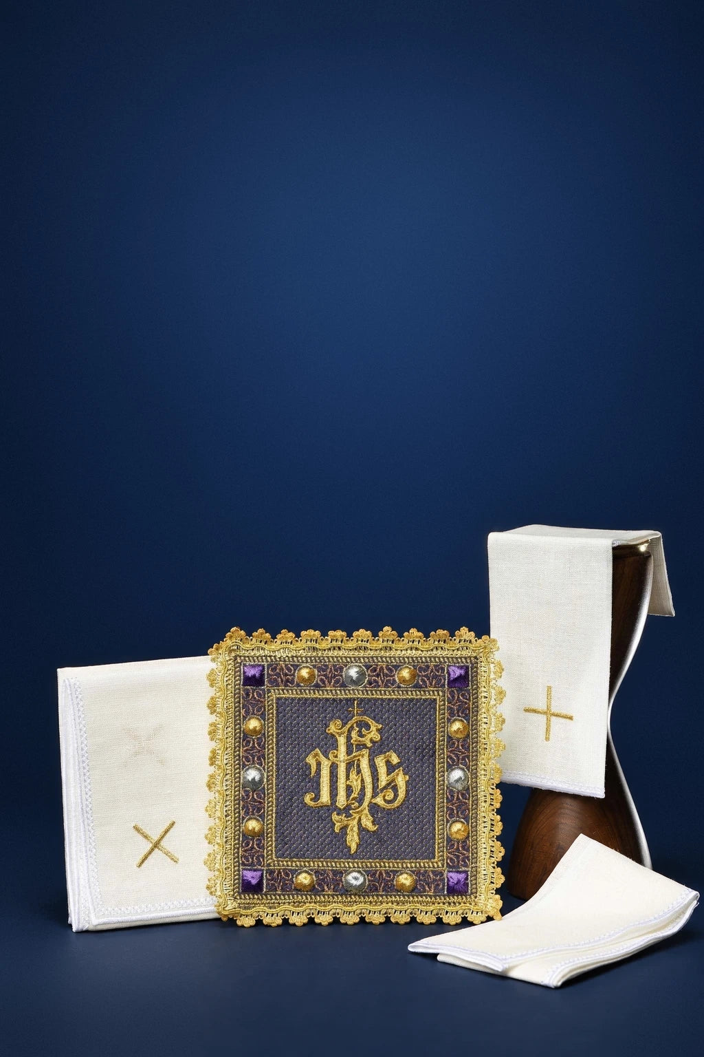 Purple altar linen set with folded purificator, pall, and corporal, featuring gold embroidered IHS and cross motifs