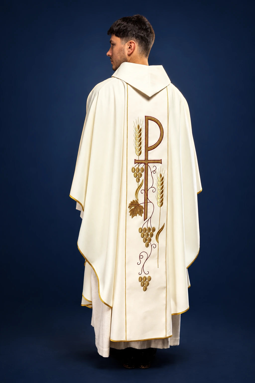 Rear three-quarter view of an ecru chasuble with pointed hood and vertical vine embroidery on the back