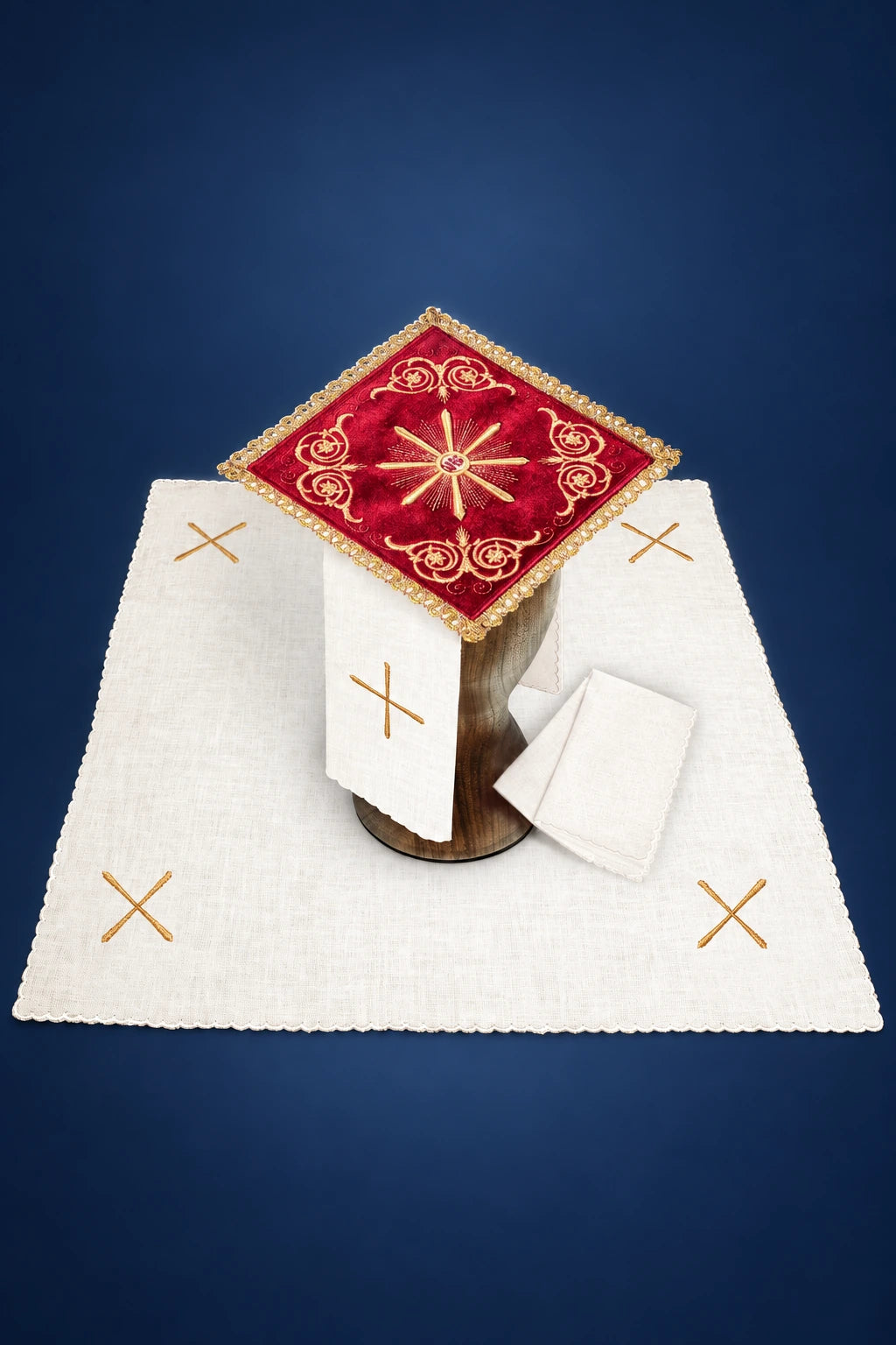 Red velvet square linen cover with embroidered Eucharistic motif on a wooden stand, surrounded by white altar cloth