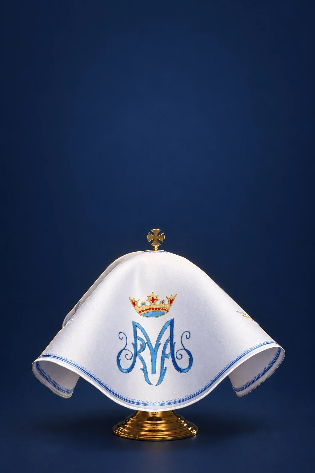 Round white ciborium veil with blue Marian monogram and crown, draped over a chalice stand